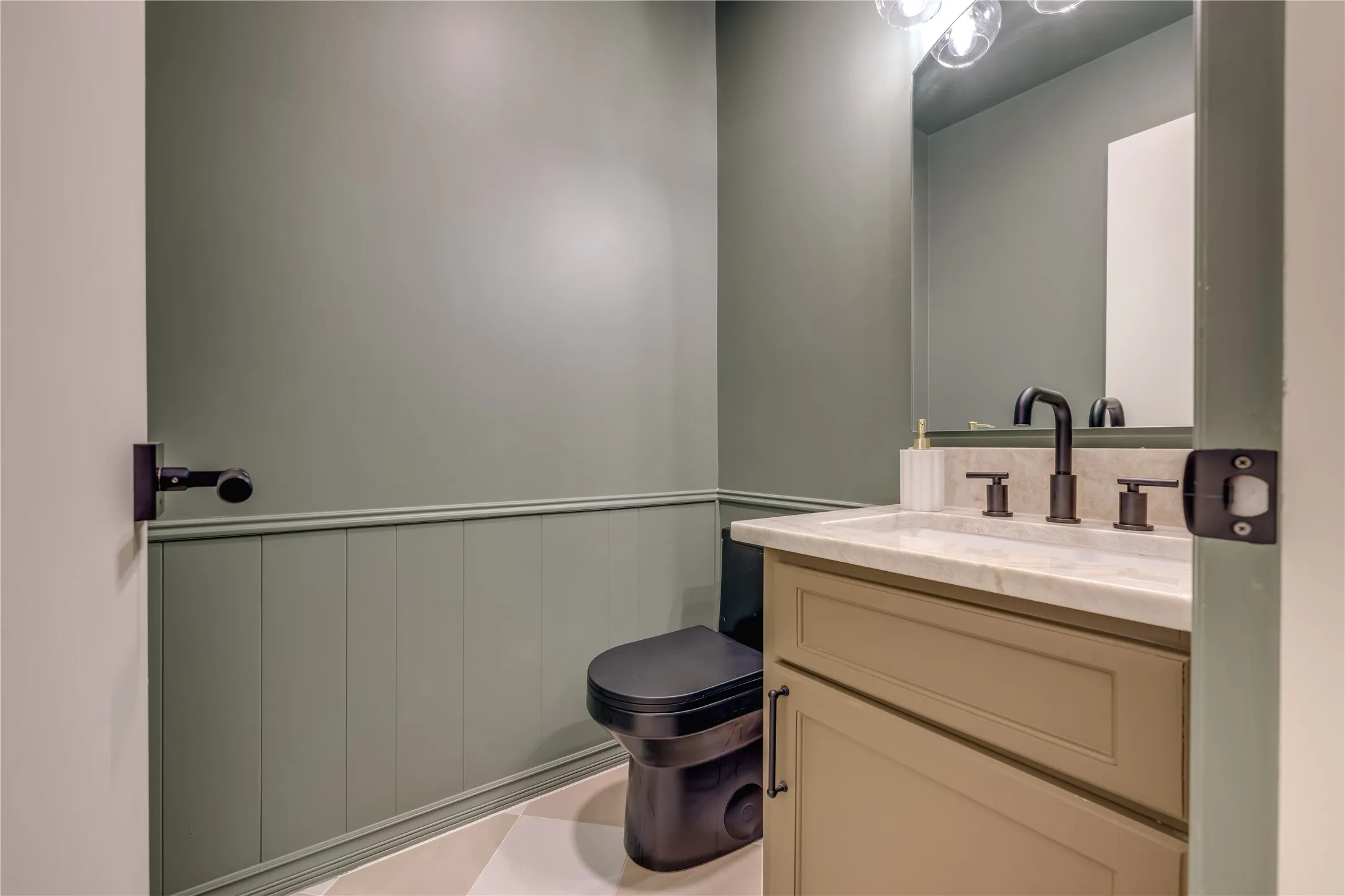Powder room featuring board and batten wainscoting, a vanity with a light-toned countertop, a black faucet, and a black toilet