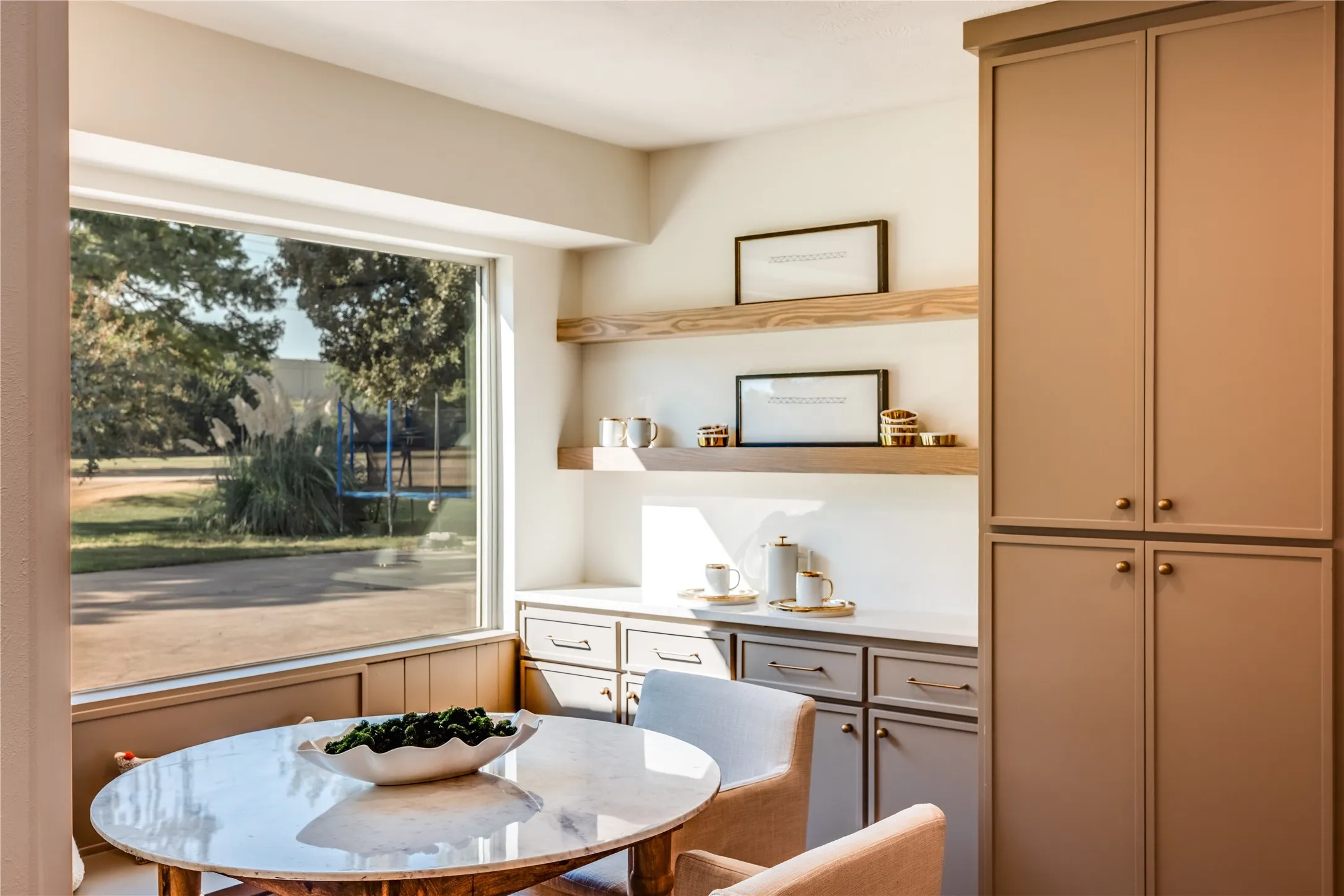 Built-in cabinetry with bronze hardware, open wood shelving, a large picture window, and a light-toned countertop