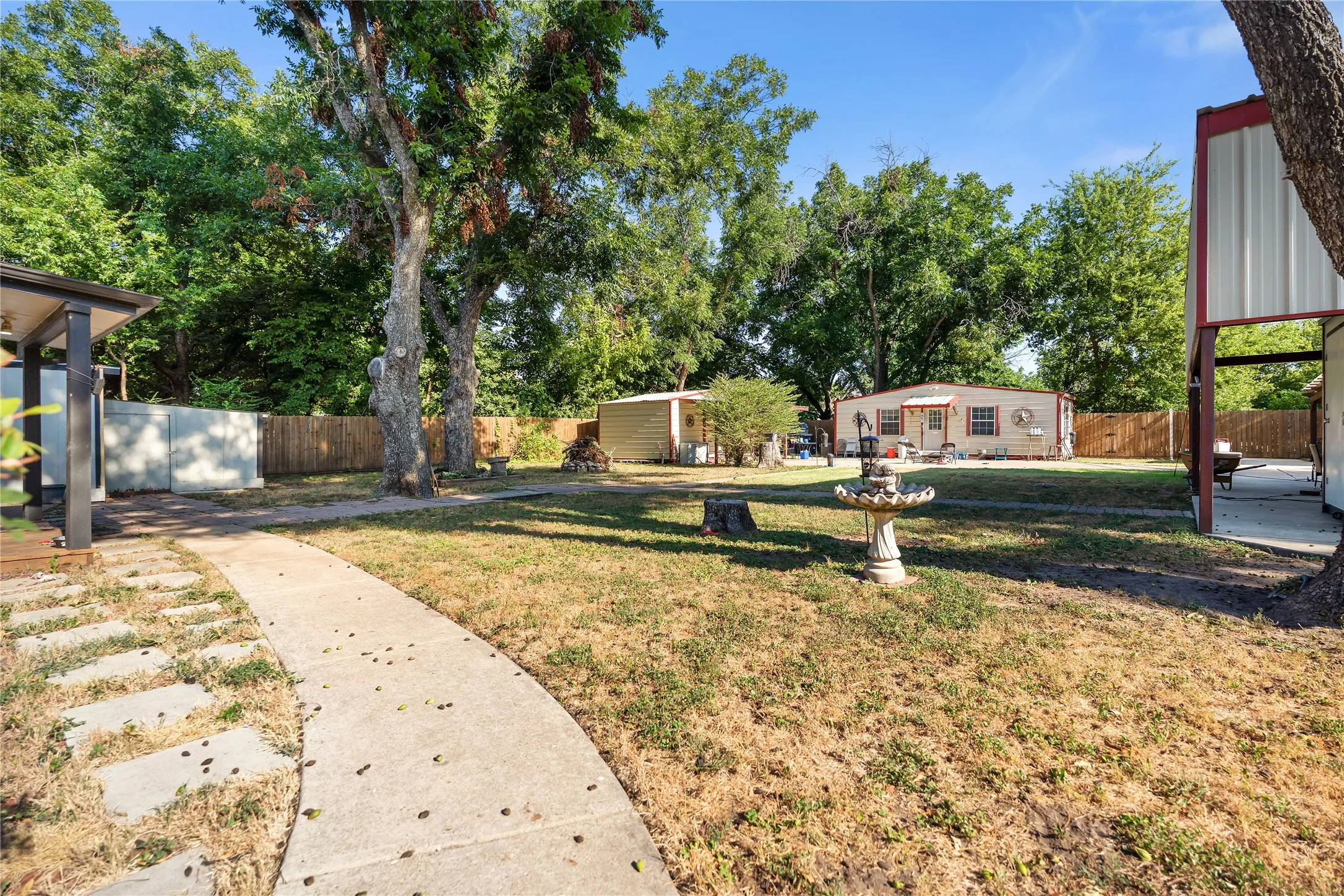 Expansive outdoor space featuring a concrete pathway, partial fencing, and mature trees