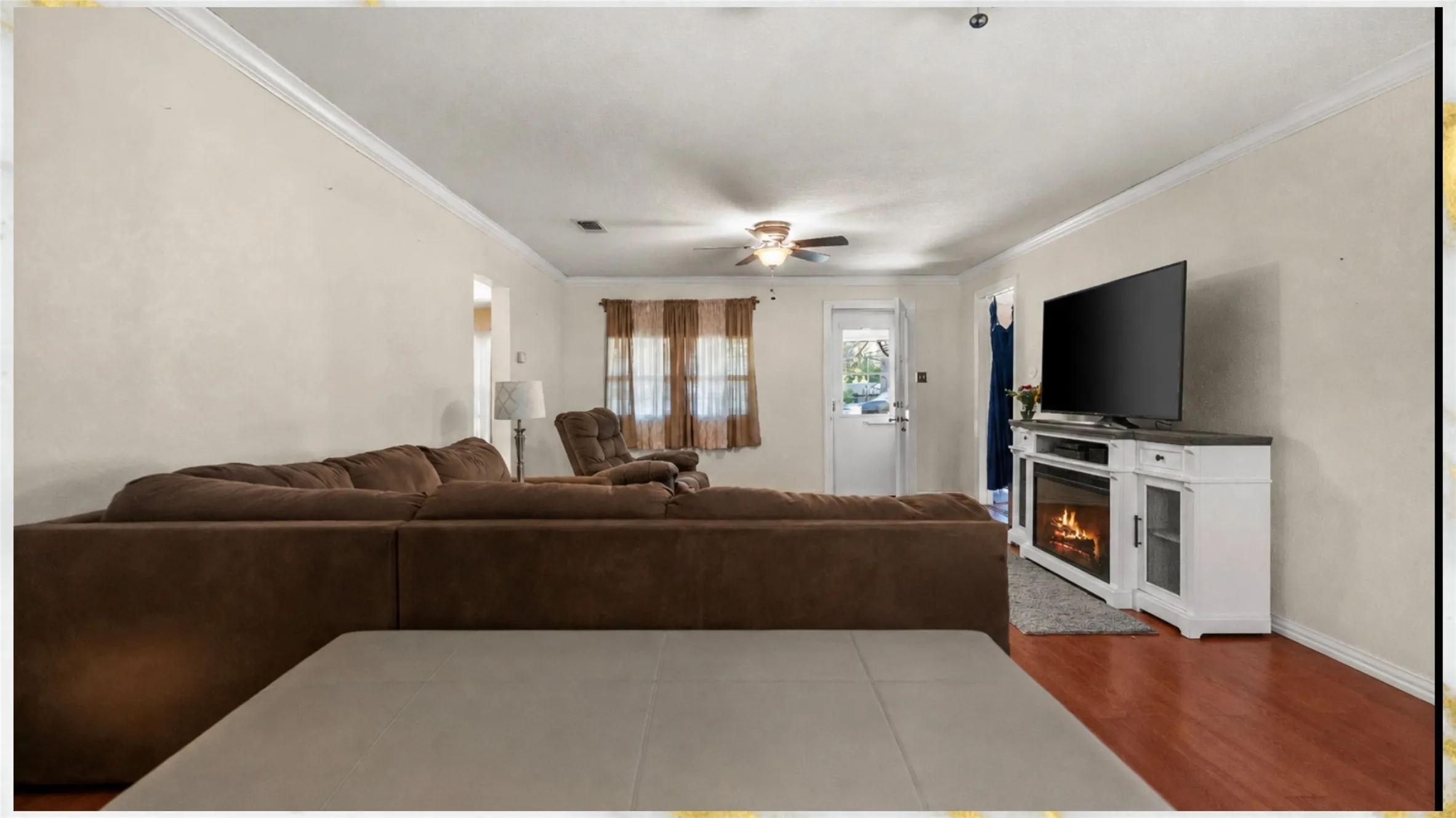 Living area with crown molding, wood-finish flooring, a ceiling fan, and a built-in media console with an electric fireplace