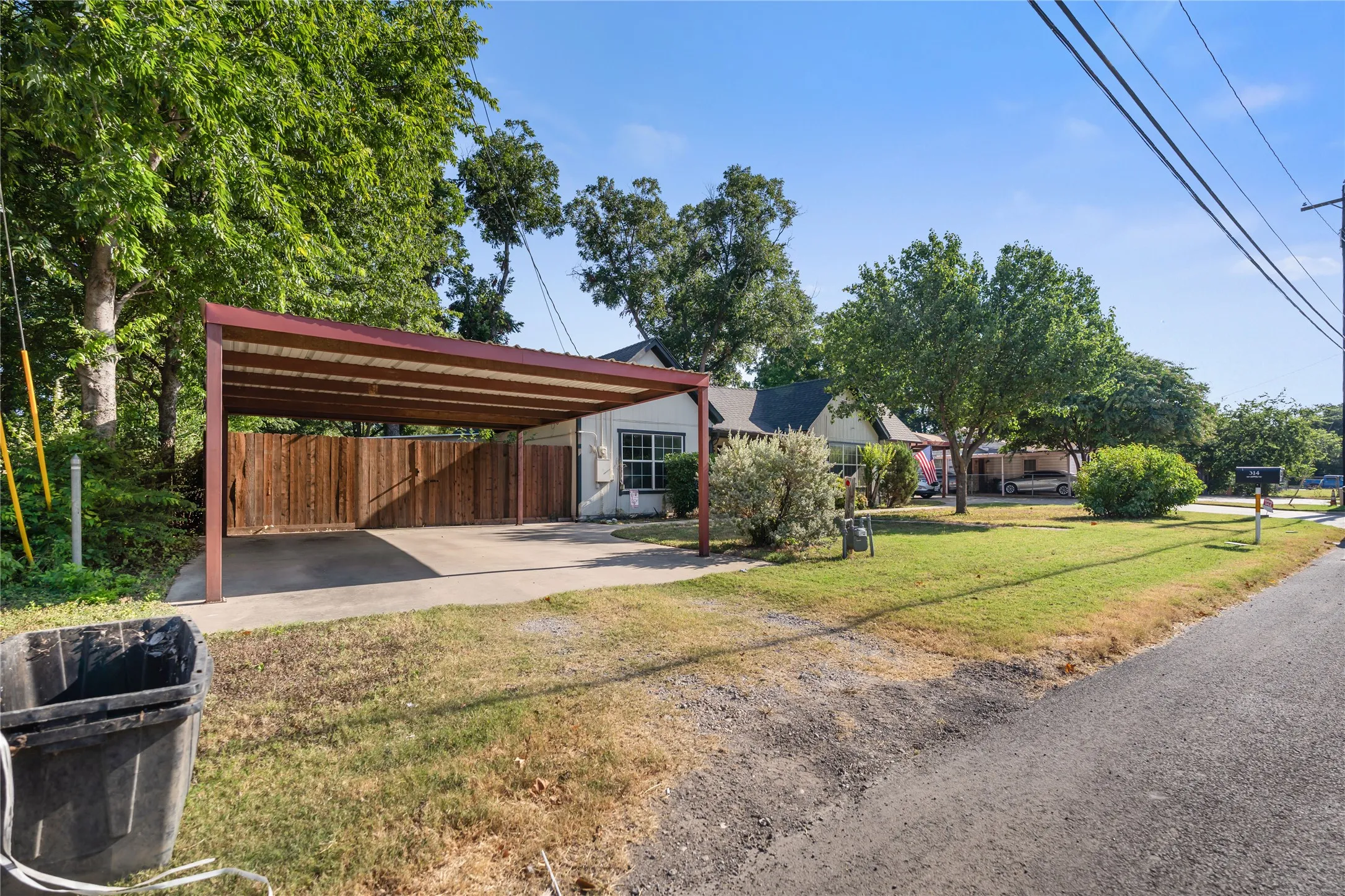 Front exterior with a covered carport, mature trees, and a concrete driveway