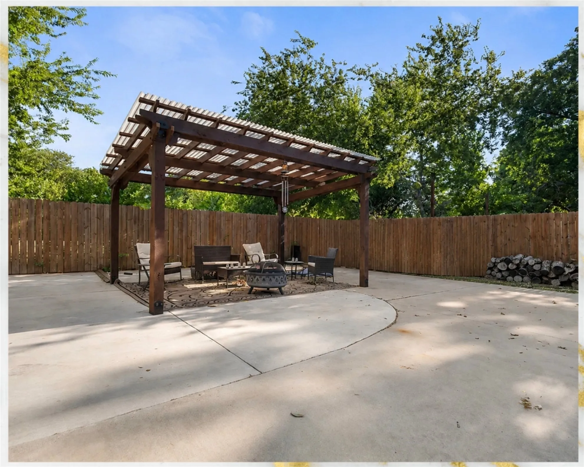 Concrete patio with a wood pergola, privacy fencing, and mature trees