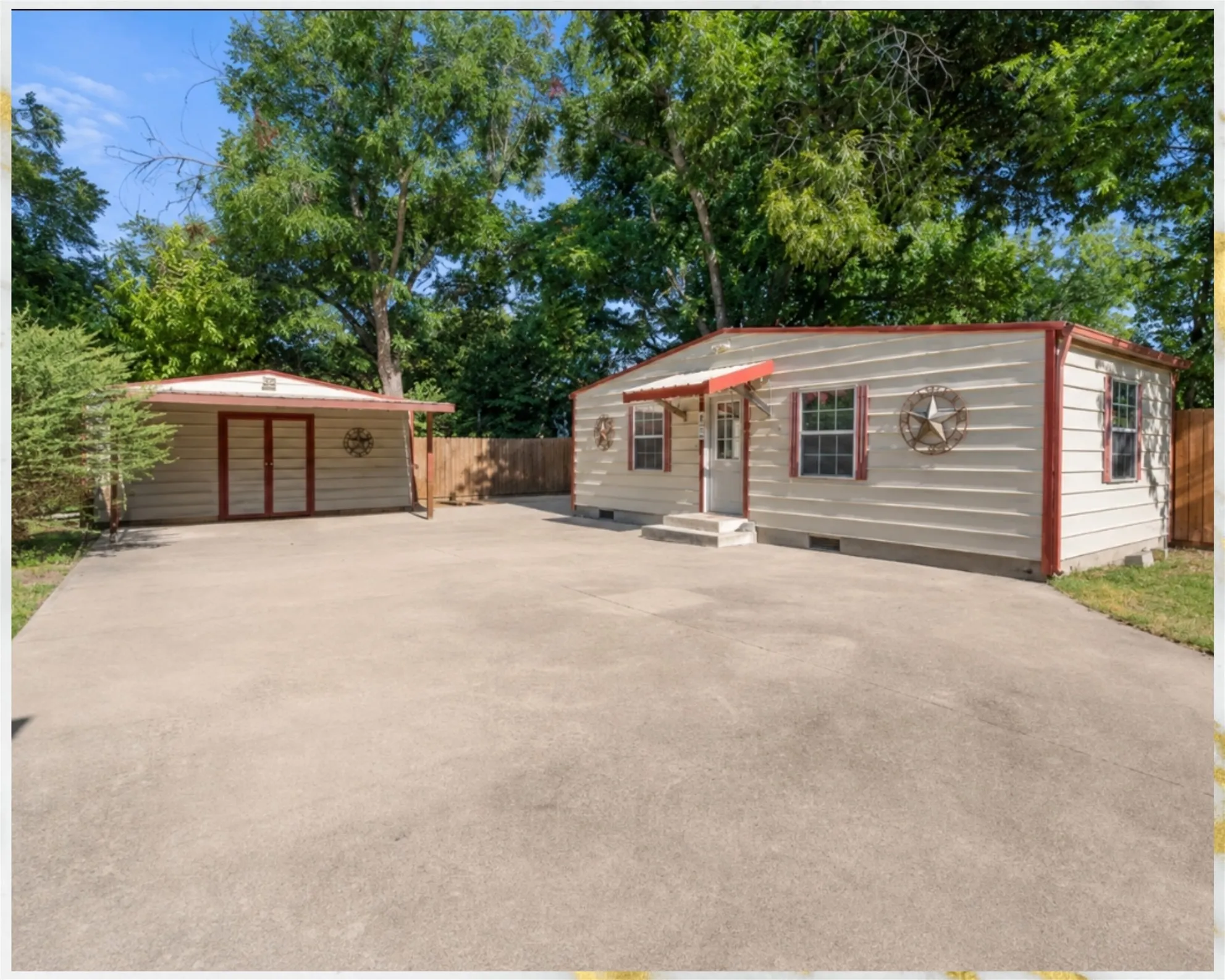 Expansive concrete driveway, detached storage building with double doors, and a residence featuring exterior siding with red trim