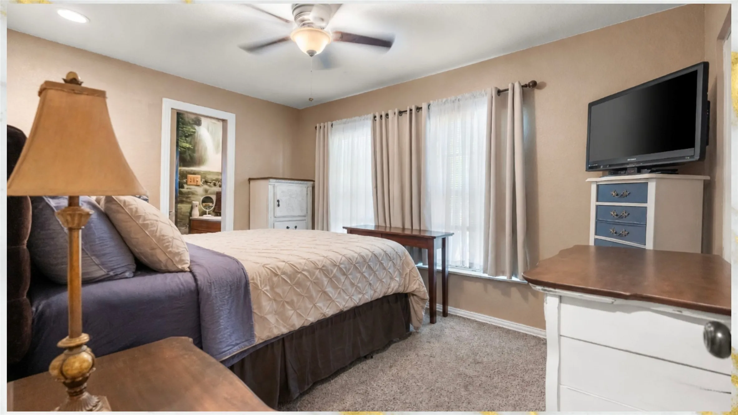 Carpeted bedroom with a ceiling fan, multiple windows, and a wall-mounted television