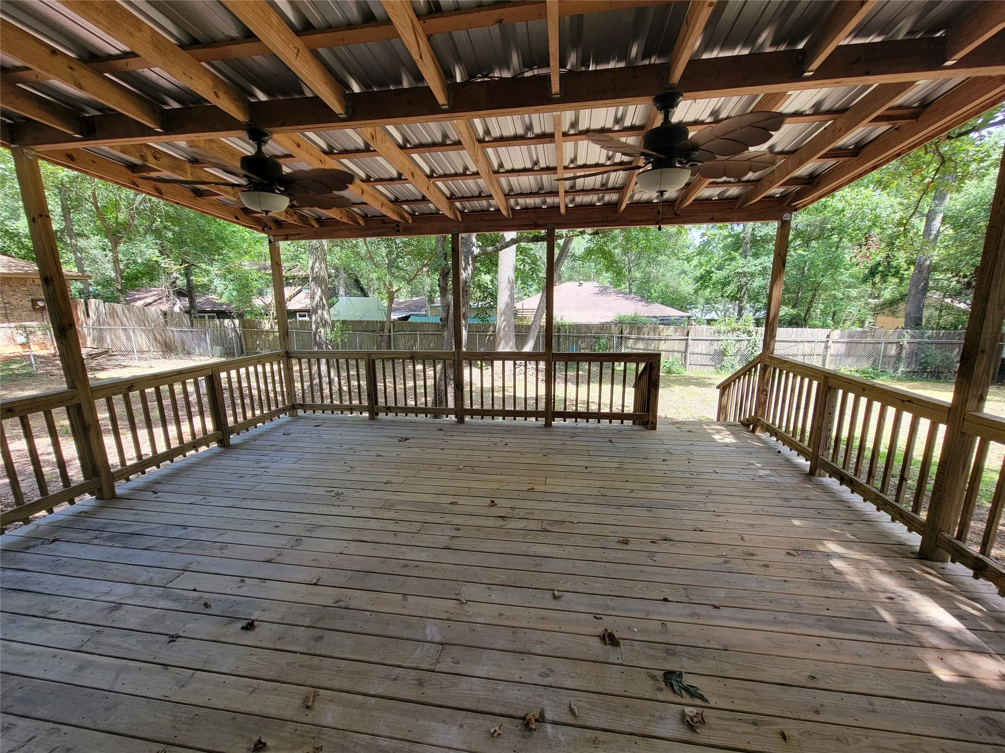 Expansive covered deck featuring wood decking, wood railings, two ceiling fans with integrated lighting, and a corrugated metal roof