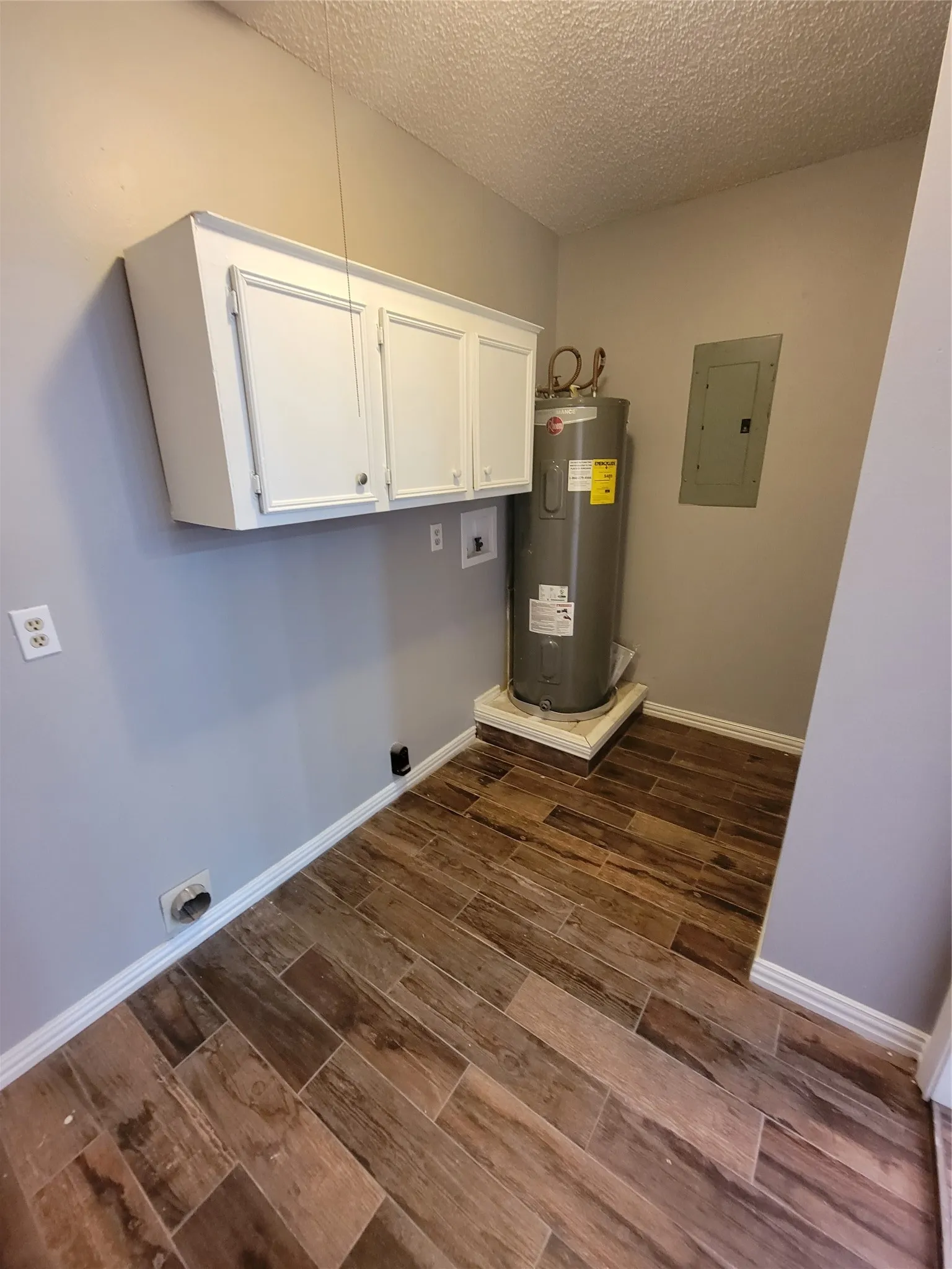Wood-finish tile flooring, white upper cabinetry, and a ceiling-mounted hot water heater