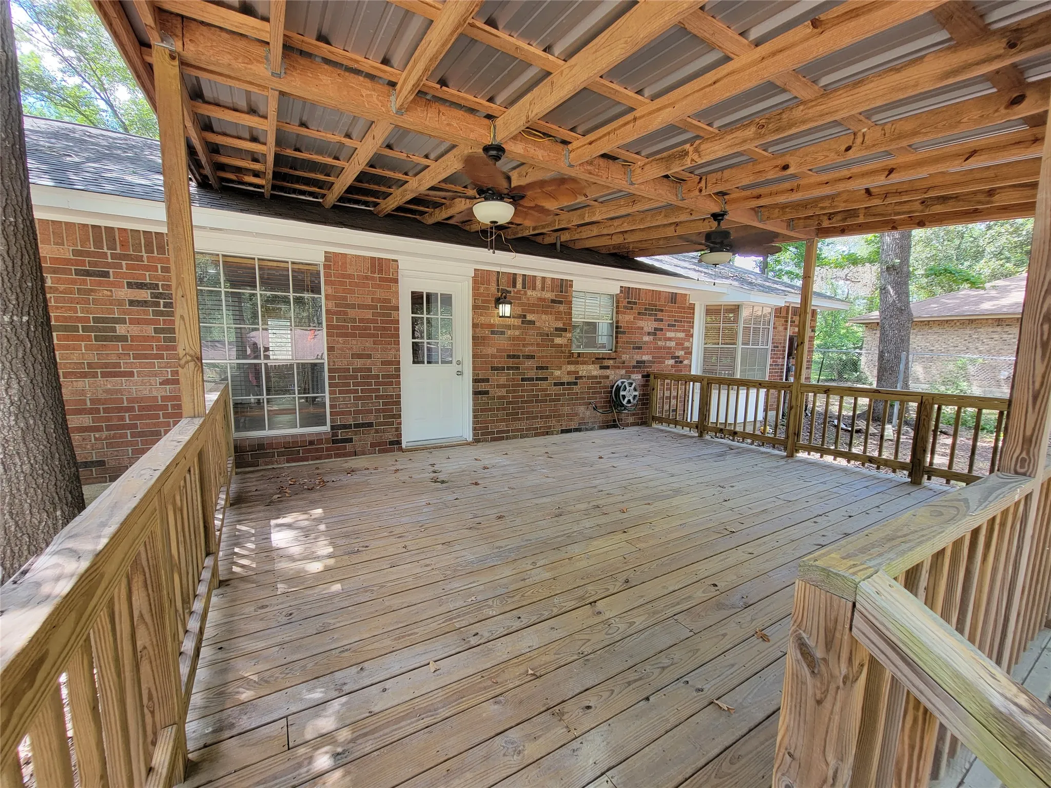Expansive wood deck with a full-length wood railing, brick exterior, and a wood-beamed covered ceiling with two ceiling fans