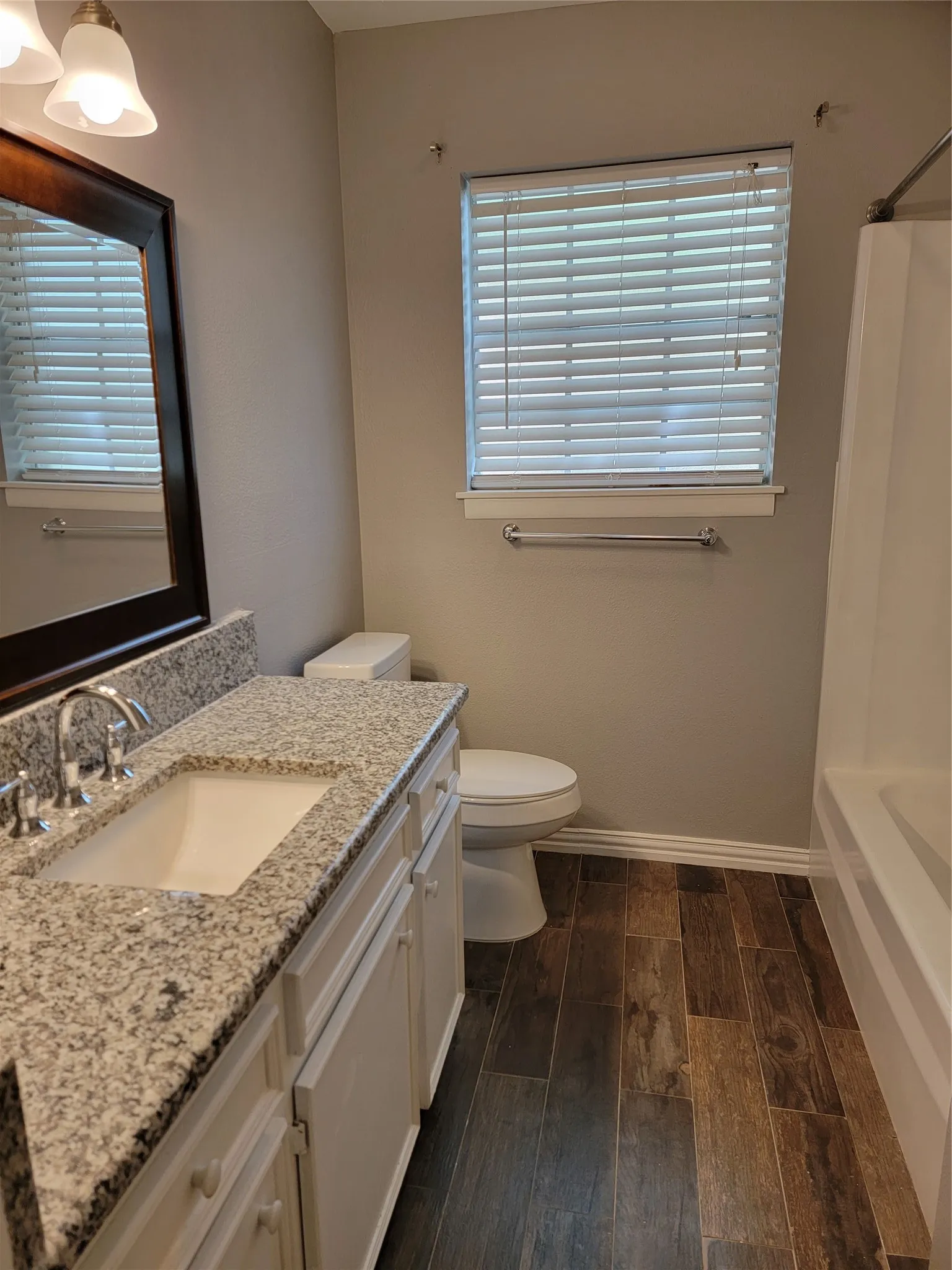 Wood-finish flooring, white vanity with granite countertop, and a built-in bathtub