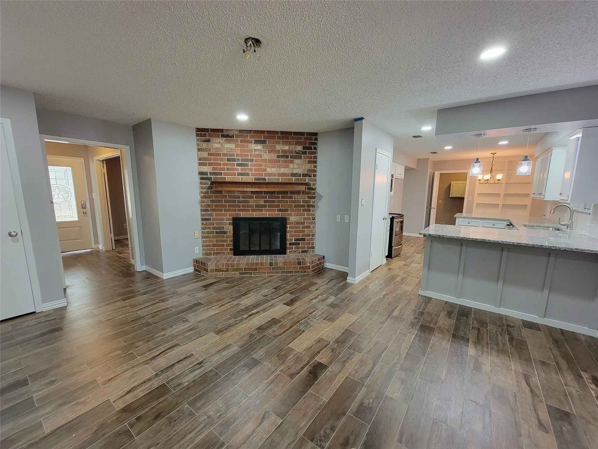 Brick-faced fireplace with wood mantel, wood-finish flooring, recessed lighting, white built-in shelving, and a kitchen island with stone countertop