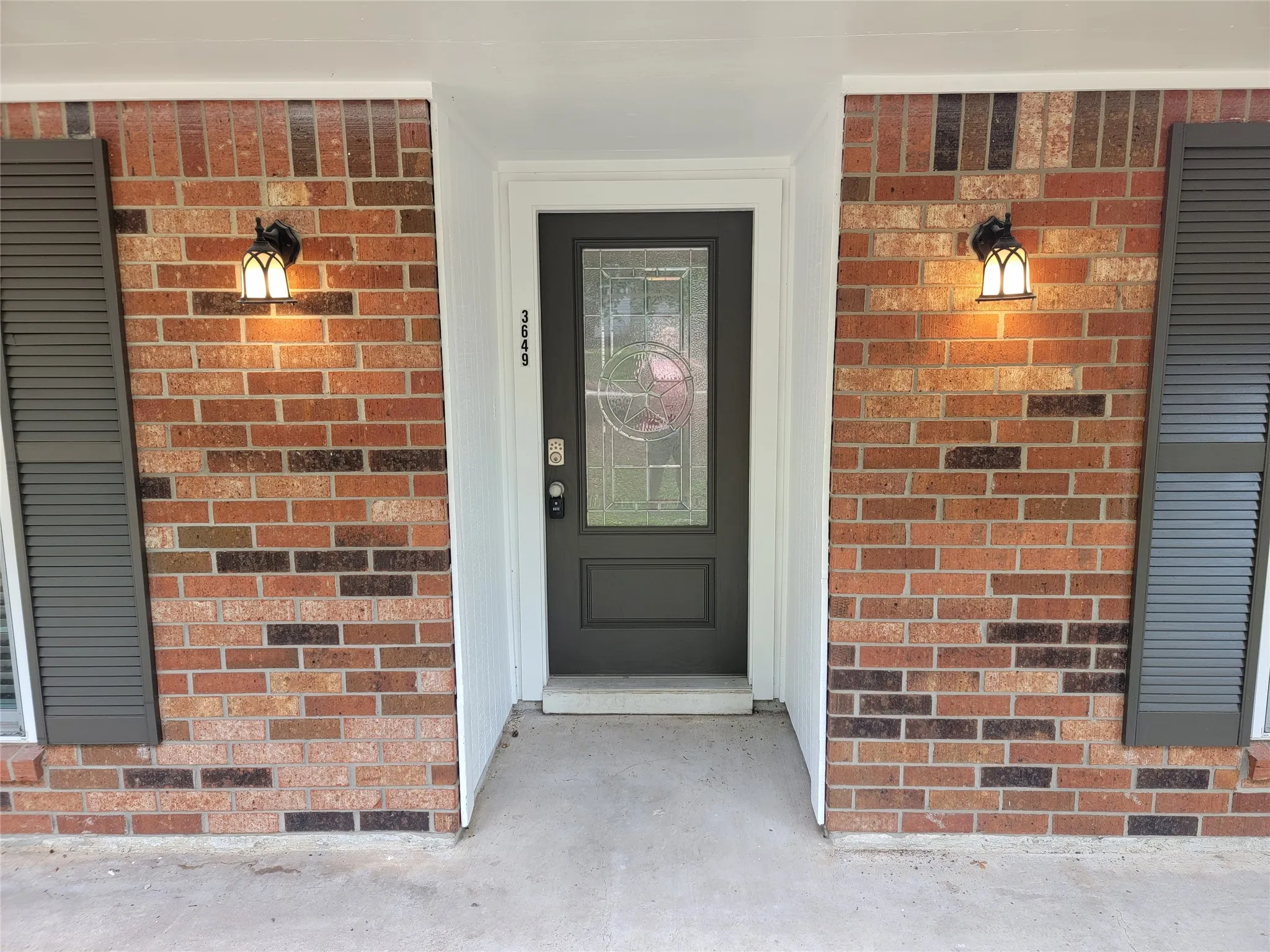 Brick exterior featuring a paneled entry door with decorative glass, dual exterior sconces, and louvered window shutters