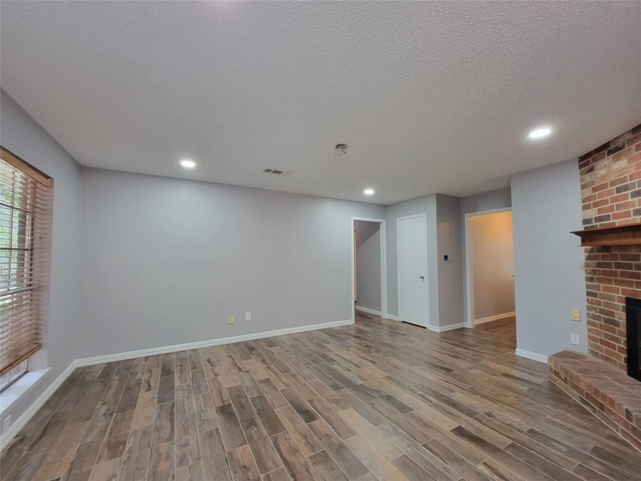 Wood-finish flooring throughout, recessed ceiling lighting, brick-clad fireplace with mantel, and white trim