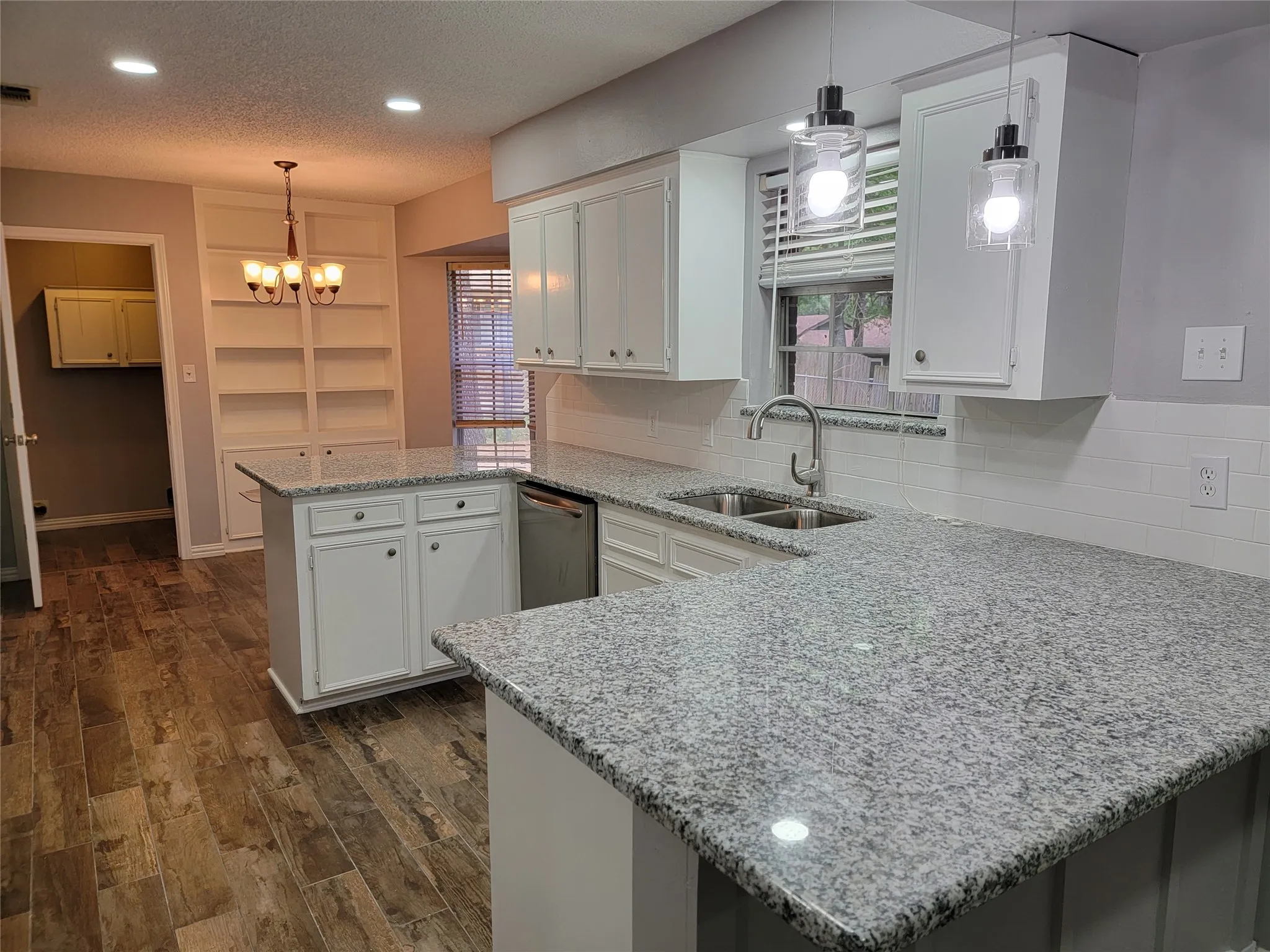 Kitchen featuring granite countertops, wood-finish flooring, white cabinetry, a built-in double basin sink, and pendant lighting