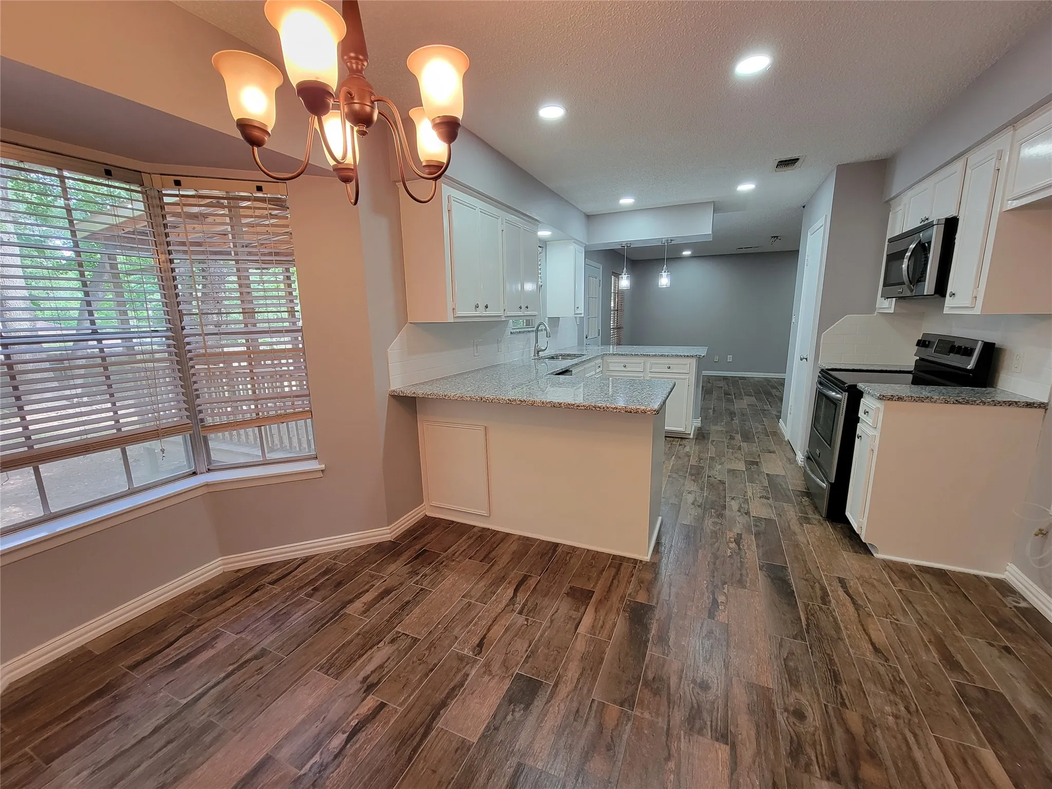 Wood-finish flooring, white cabinetry, granite countertops, stainless steel appliances, and recessed lighting