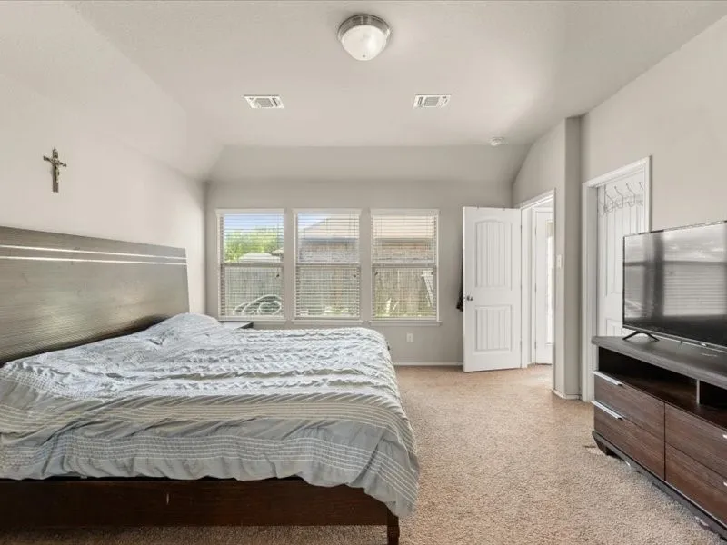 Vaulted ceiling, arched doorway, three windows with blinds, and neutral carpet flooring