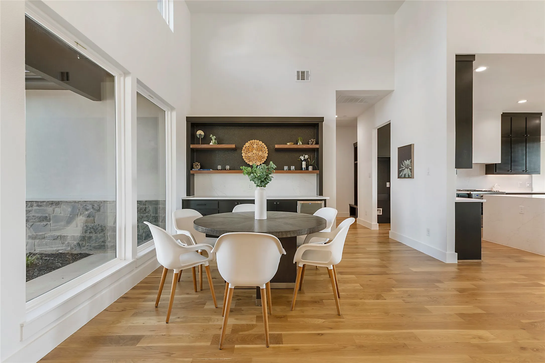 High ceilings, wood-finish flooring, built-in shelving, large windows, and a partial view of the kitchen with dark cabinetry
