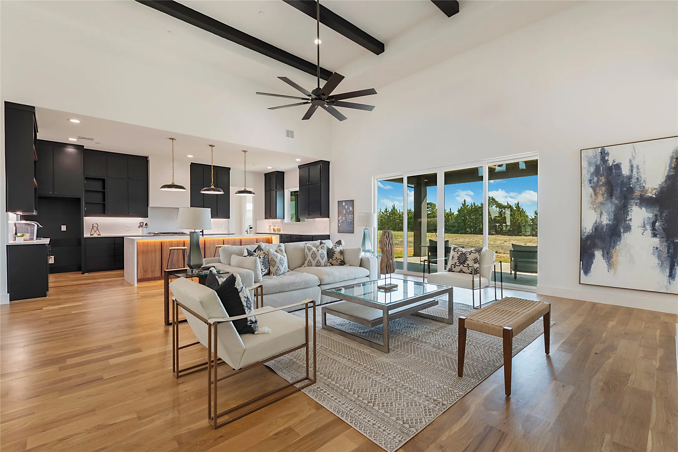 Vaulted ceiling with exposed beams, wood-finish flooring, kitchen island with integrated lighting, expansive sliding glass doors, and recessed lighting