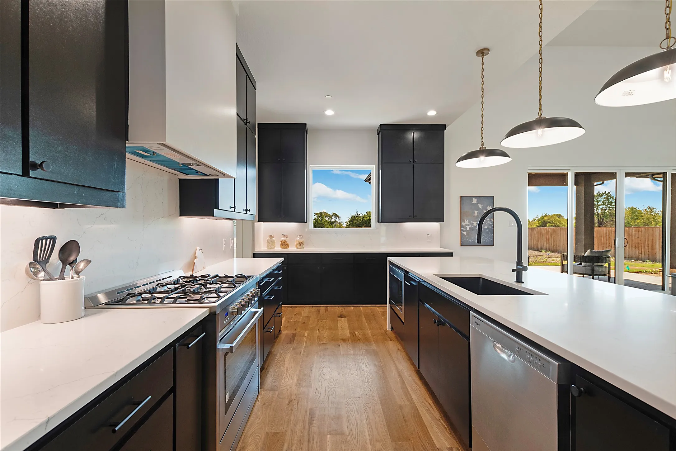 Gourmet kitchen featuring a gas range, stainless steel appliances, dark cabinetry, light countertops, and wood-finish flooring