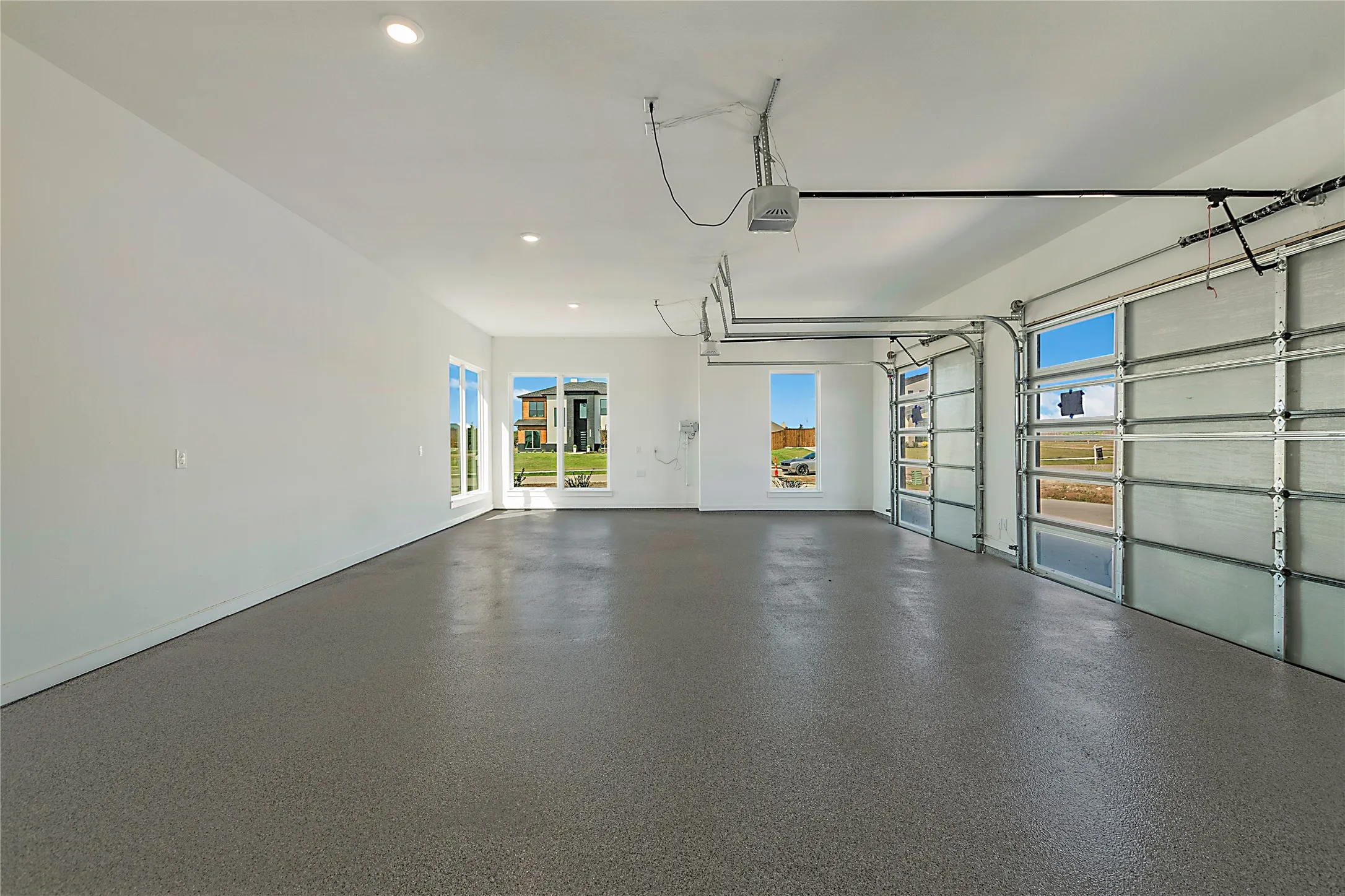 Spacious garage featuring polished concrete flooring, dual glass panel garage doors with natural light, recessed ceiling lighting, and glass-pane entry doors opening to the home's interior