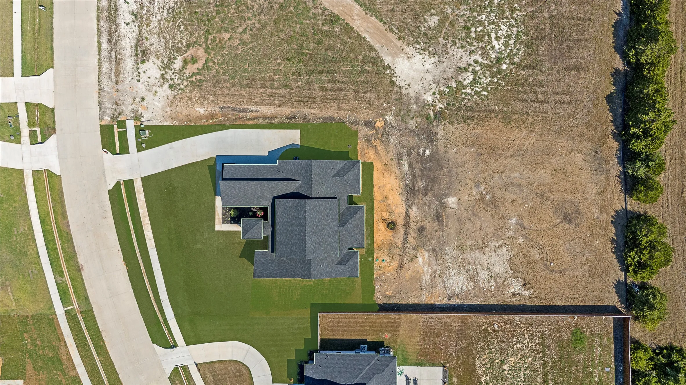 Expansive lot featuring a newly constructed residence with a dark shingle roof, green lawn, and concrete driveway