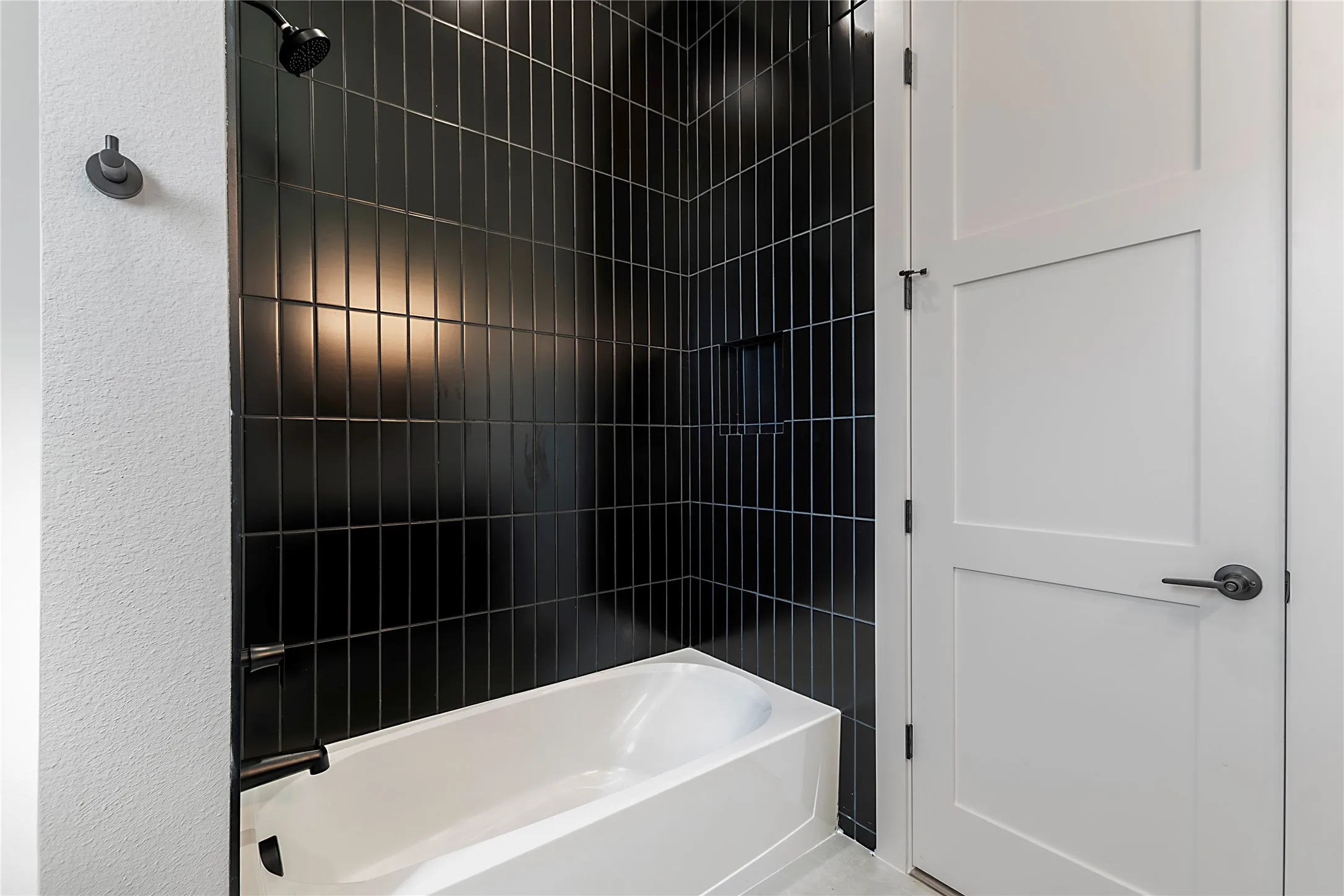 Black subway tile shower surround with a built-in niche, matte black shower fixtures, and a white bathtub