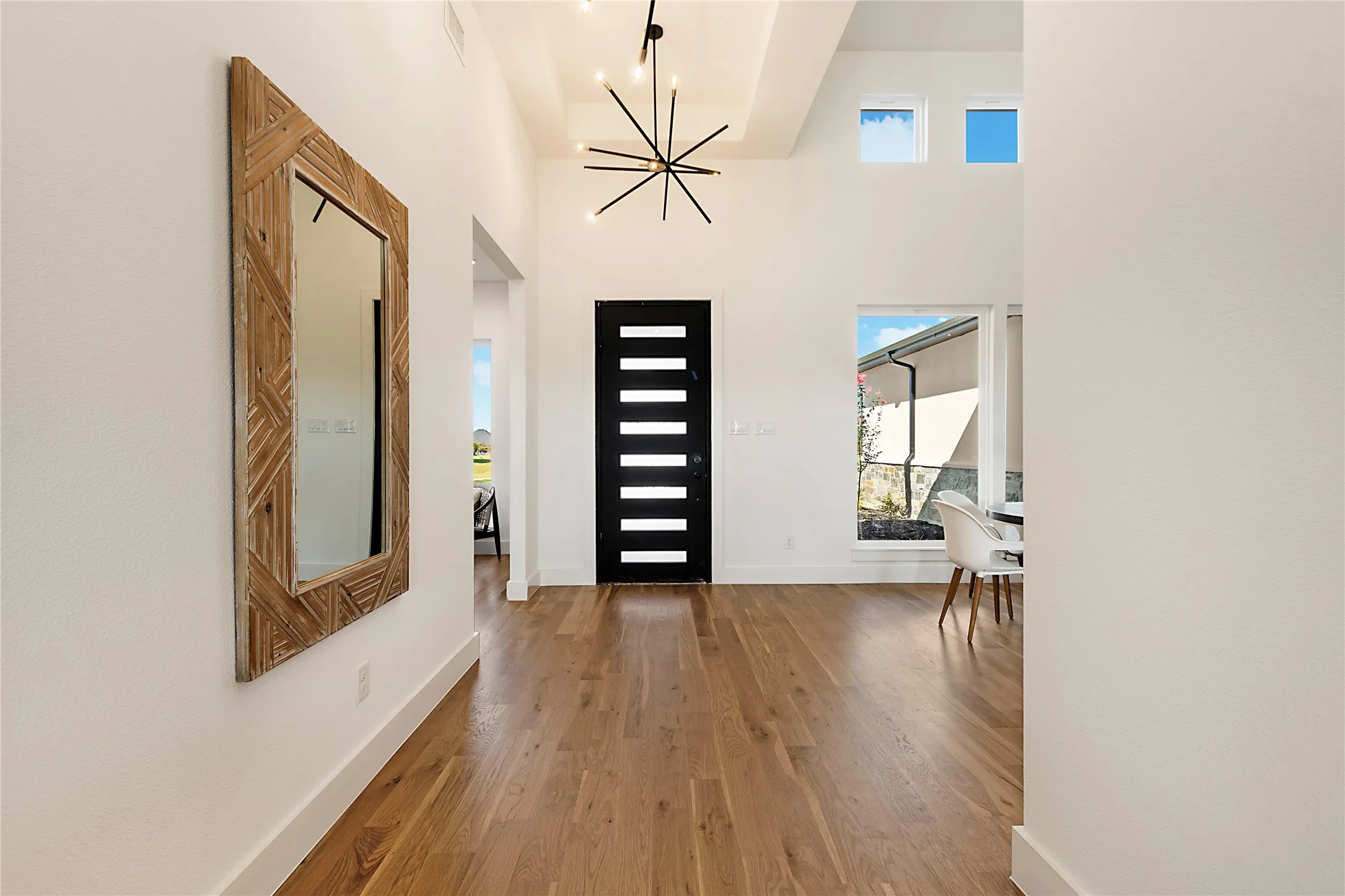 Vaulted ceiling, wood-finish flooring, modern black entry door with horizontal lites, large picture window, and transom windows
