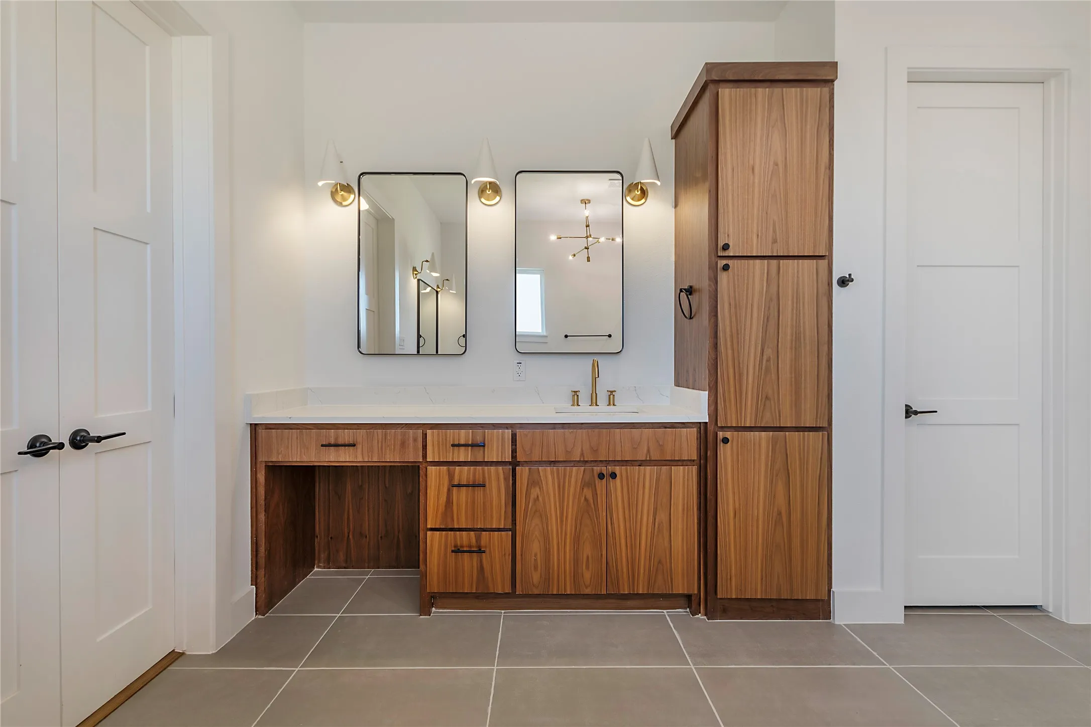 Dual framed mirrors with sconce lighting, wood-finish cabinetry, built-in storage tower, quartz-finish countertop, and large format tile flooring