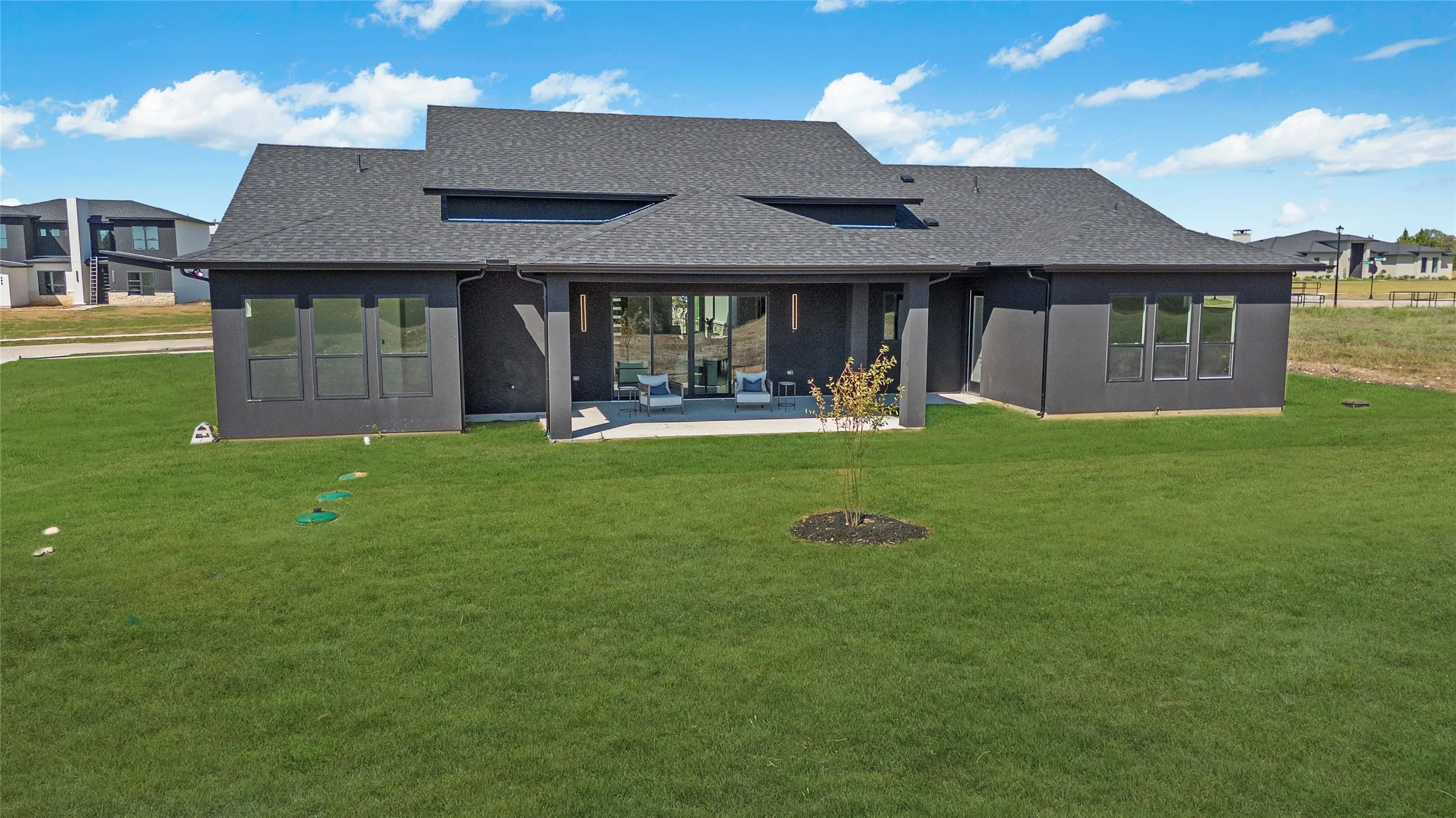 Expansive green lawn, dark gray exterior, large sliding glass door, covered patio, and contemporary roofline
