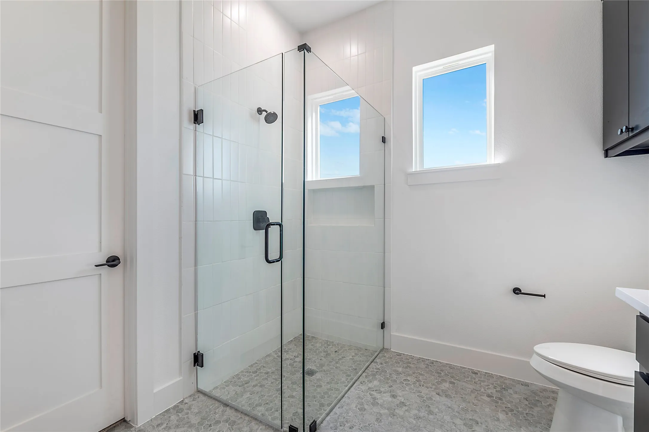 Glass-enclosed shower with white subway tile, a built-in shower niche, and a contrasting dark-finish rain shower head