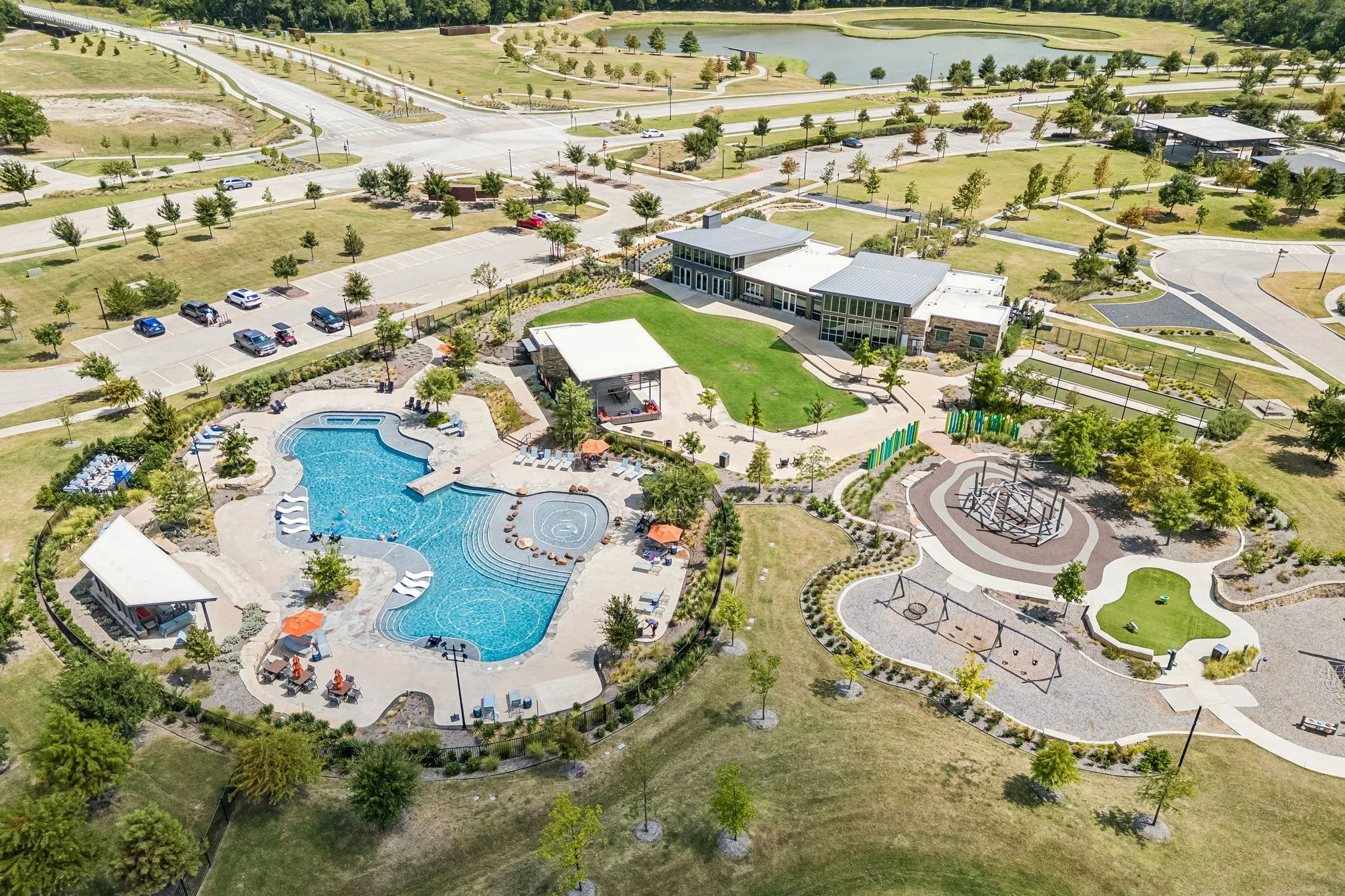 Expansive aquatic area, covered outdoor seating, large recreational green space, modern architectural clubhouse, and dedicated play area