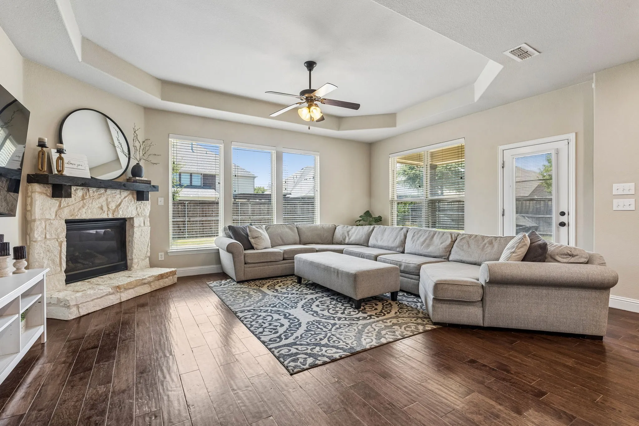 Open concept living room featuring a tray ceiling, a stone fireplace and a ceiling fan
