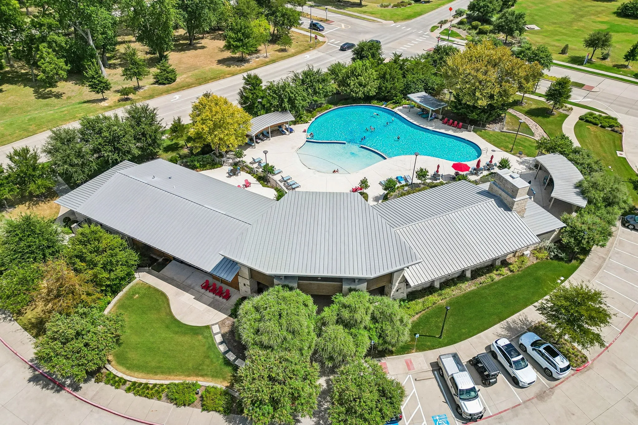 Community center with a large swimming pool, an expansive parking area, and mature landscaping