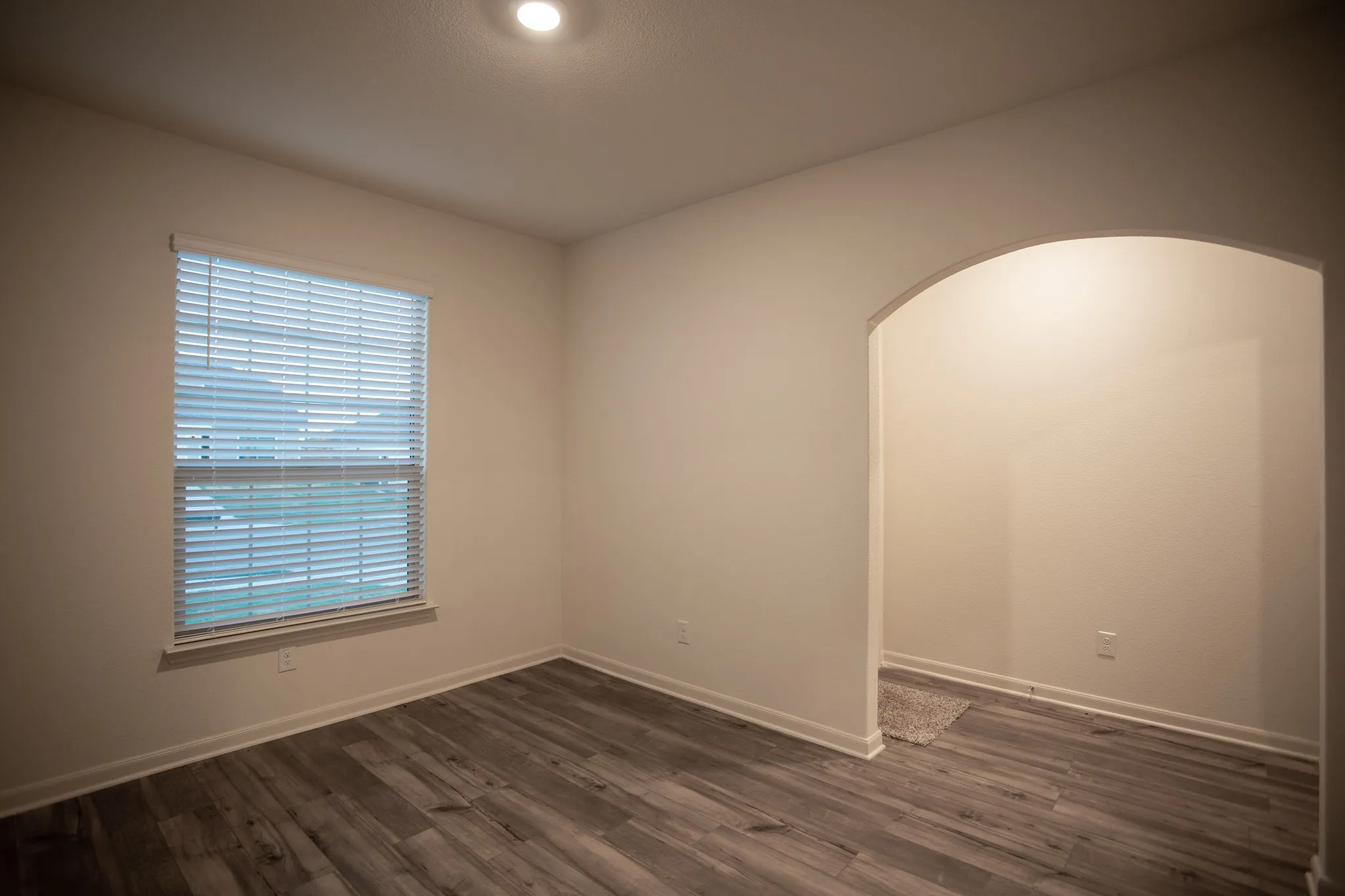 Recessed ceiling lighting, wood-finish flooring, single window with blinds, and an arched doorway