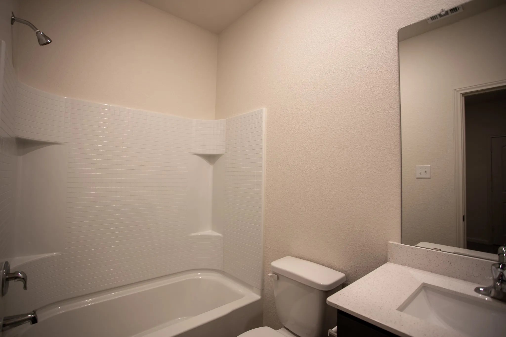 Bathtub with integrated shelving, chrome shower fixture, vanity with light-colored countertop, and a built-in mirror