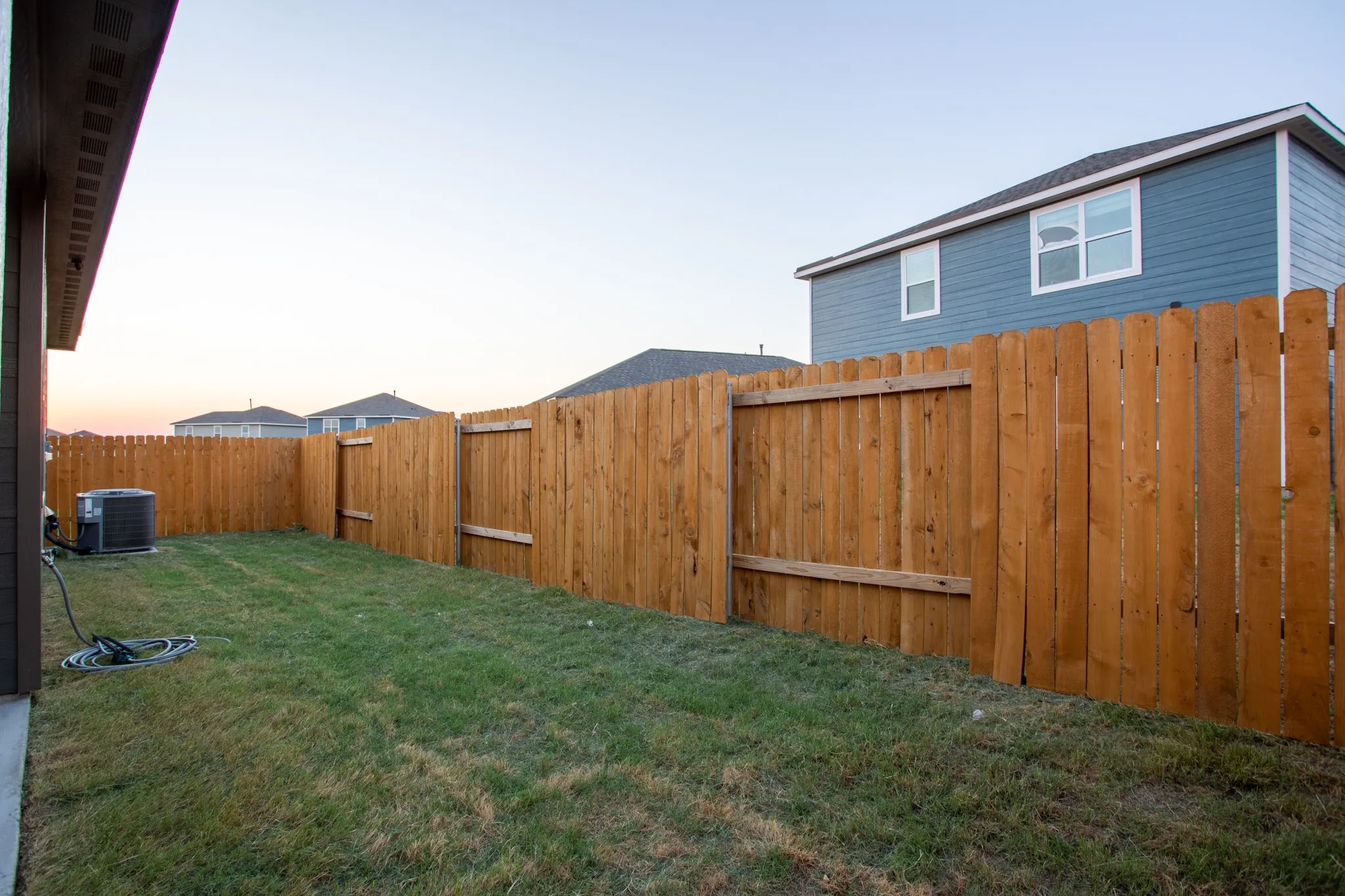 Manicured lawn, full perimeter wood fencing, and central air conditioning unit