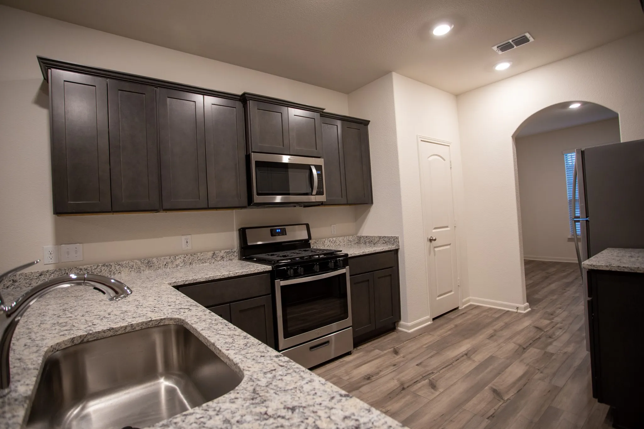 Kitchen featuring wood-finish flooring, dark cabinetry, stainless steel appliances, and light-toned countertops