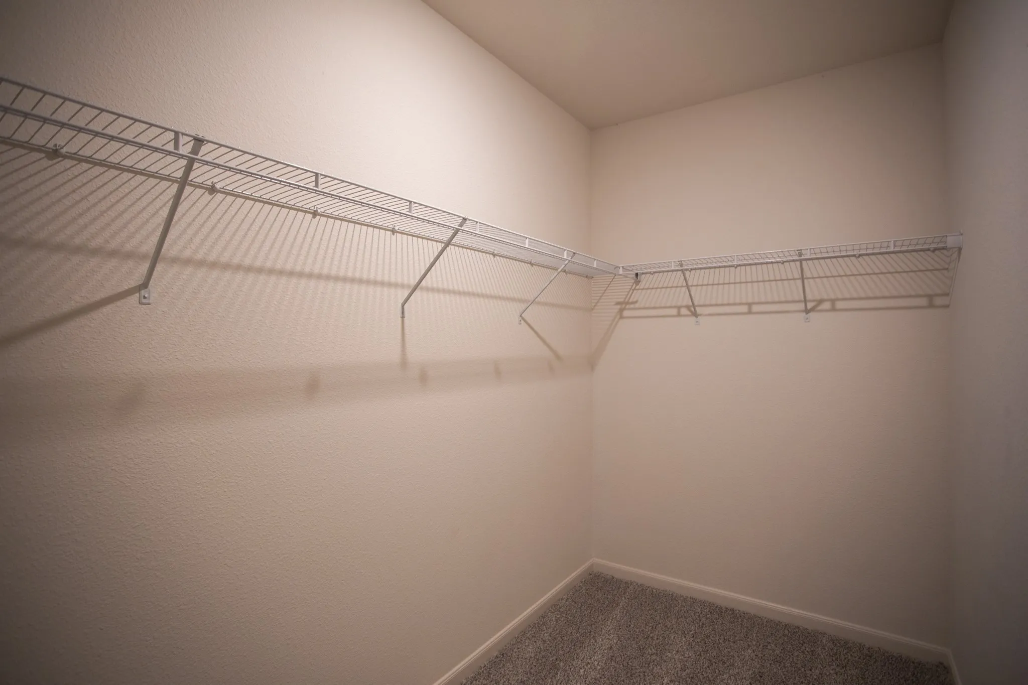 Built-in wire shelving system, L-shaped configuration, light-colored wall finish, and carpet flooring
