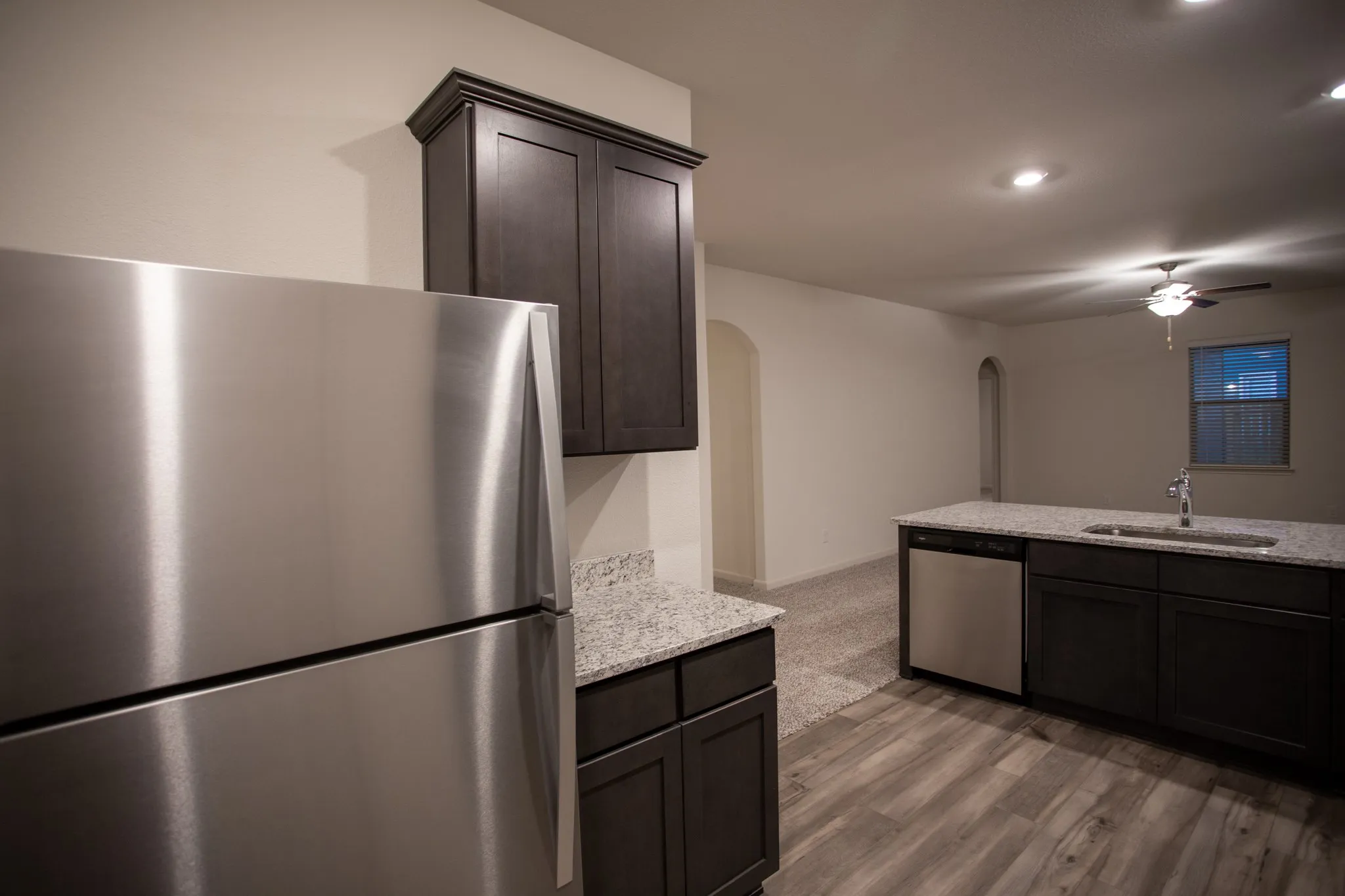 Contemporary kitchen featuring wood-finish flooring, dark wood cabinetry, light-toned granite countertops, and stainless steel appliances