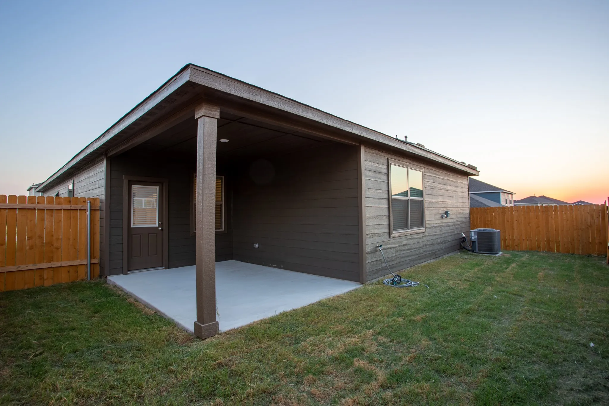 Covered patio with a concrete slab, dark brown siding, and a wooden privacy fence