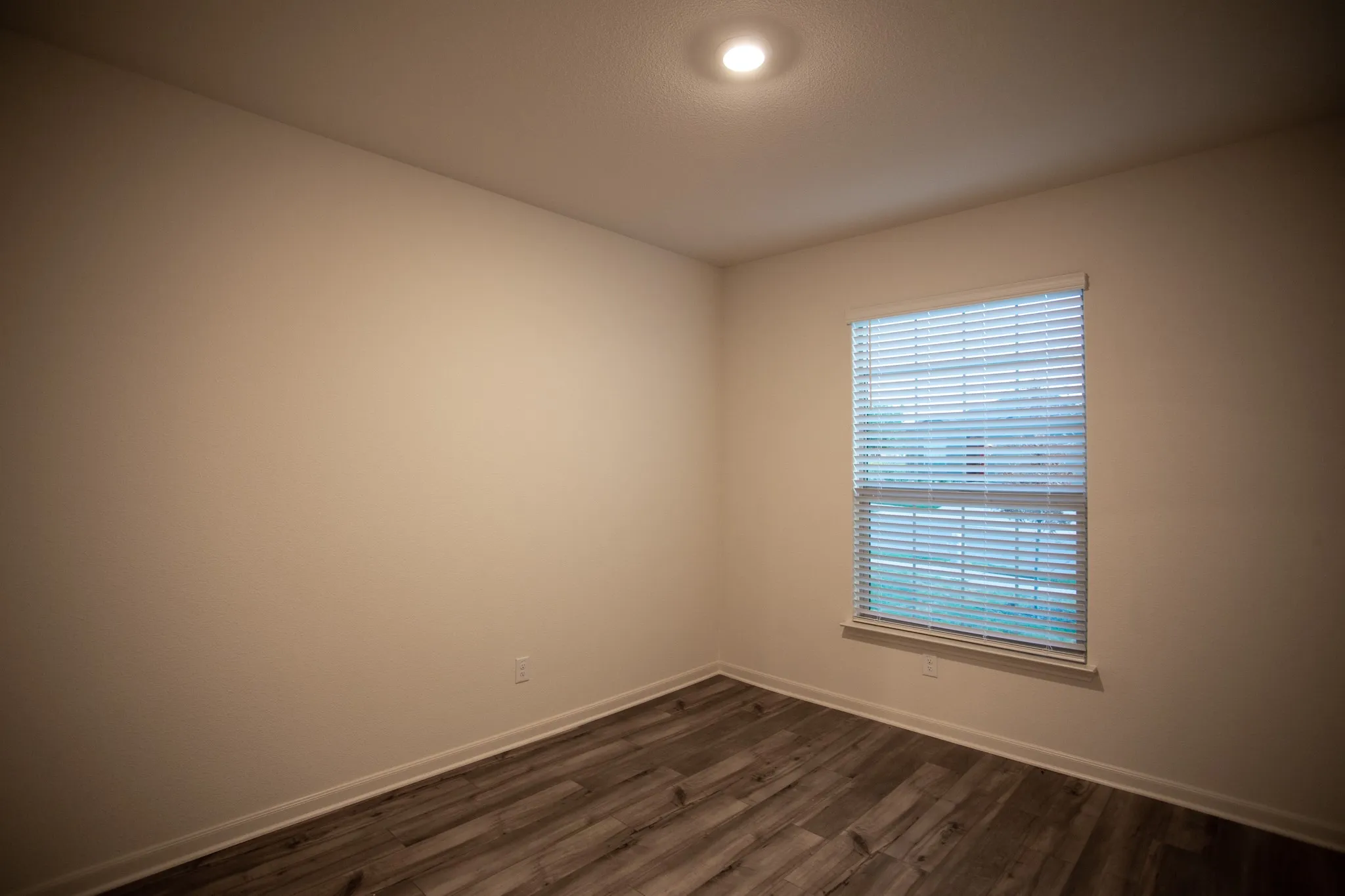 Recessed ceiling lighting, wood-finish flooring, and a single window with blinds