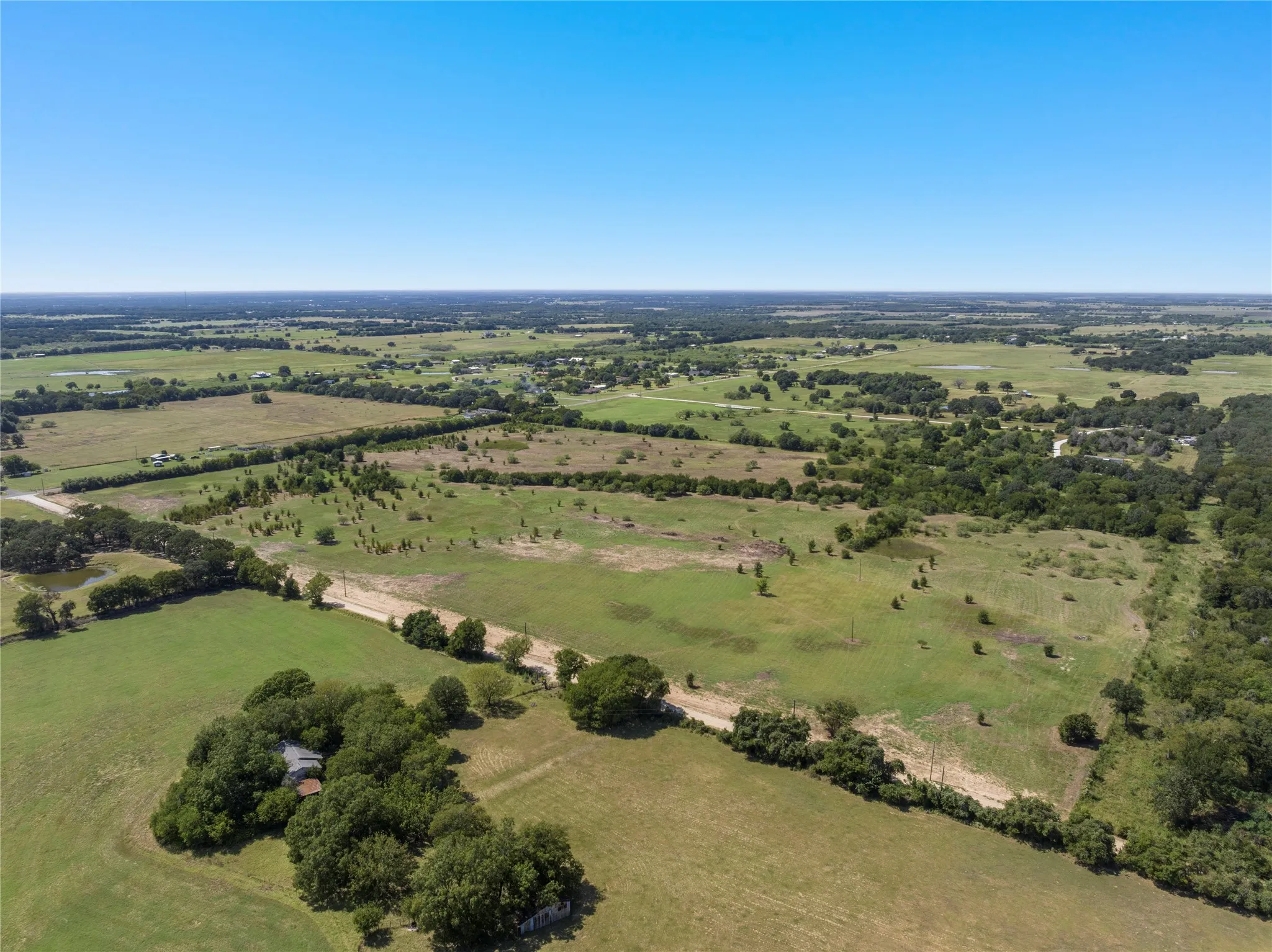 Expansive acreage with a mix of pasture and scattered trees, featuring clear skies overhead