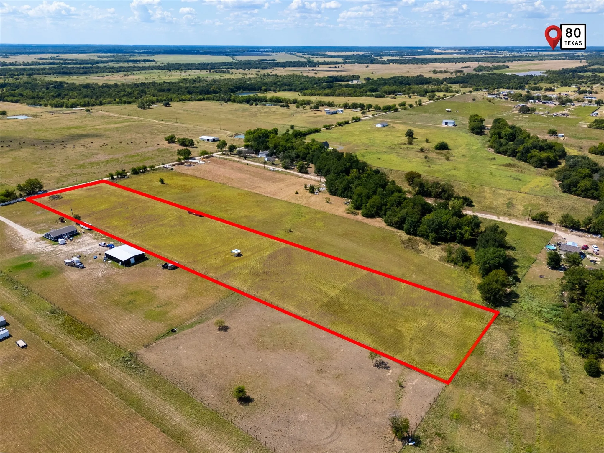 Expansive cleared land parcel with defined red-lined boundaries, featuring scattered trees and a distant rural landscape
