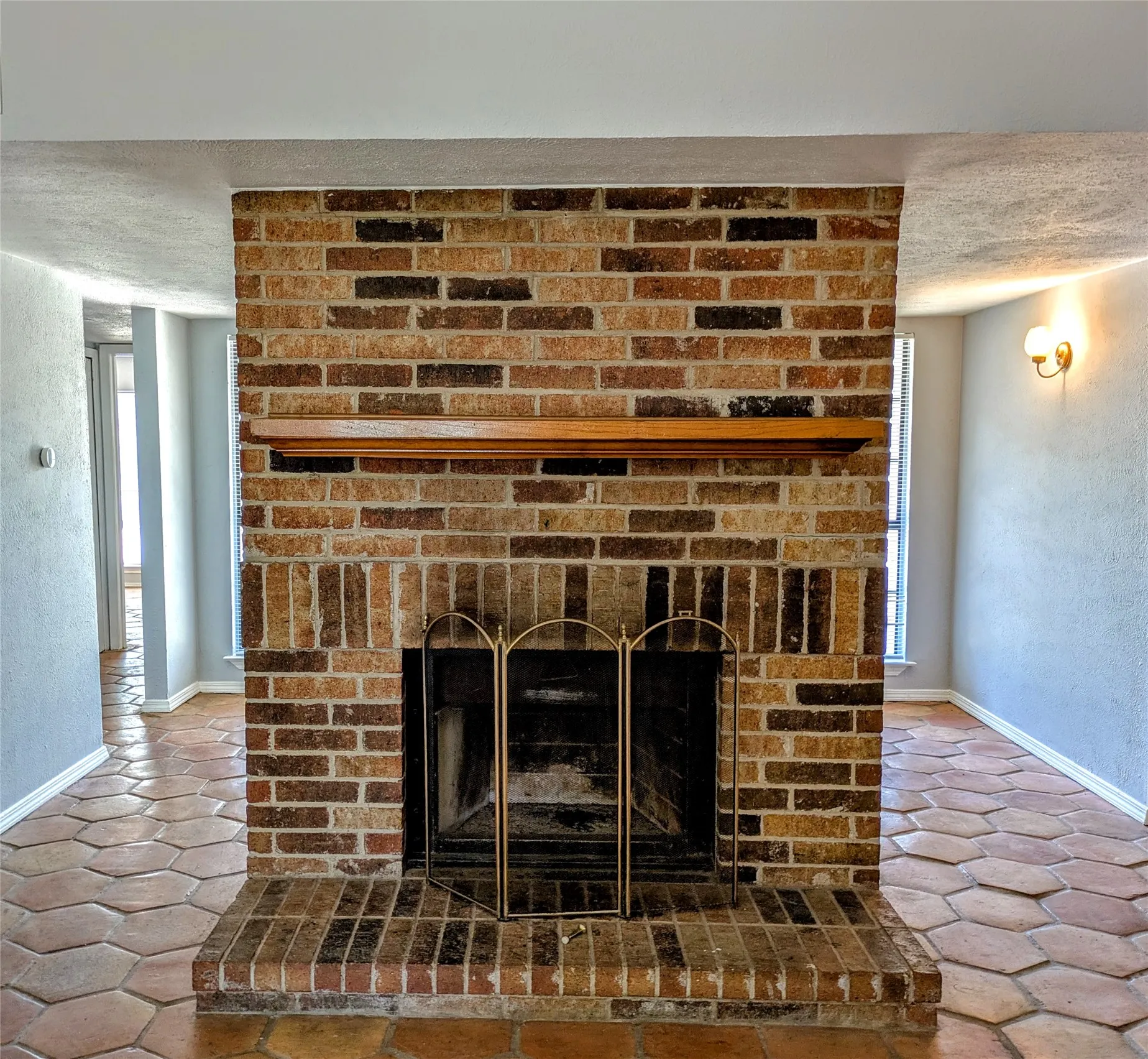 Brick fireplace with a wood mantle, a metal screen, and a hearth, featuring hexagonal tile flooring