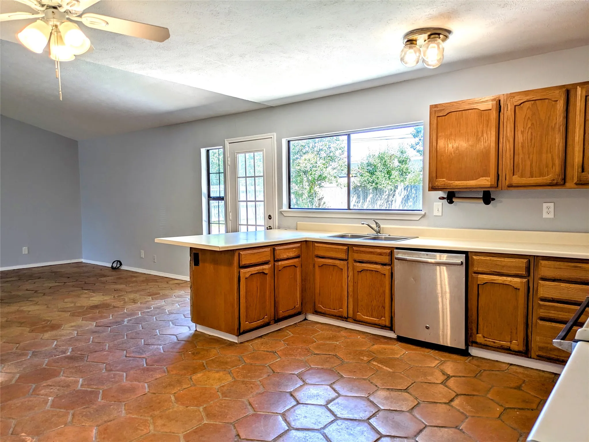 Hexagonal tile flooring, warm wood cabinetry, stainless steel dishwasher, kitchen island with countertop, and a ceiling fan with integrated lighting