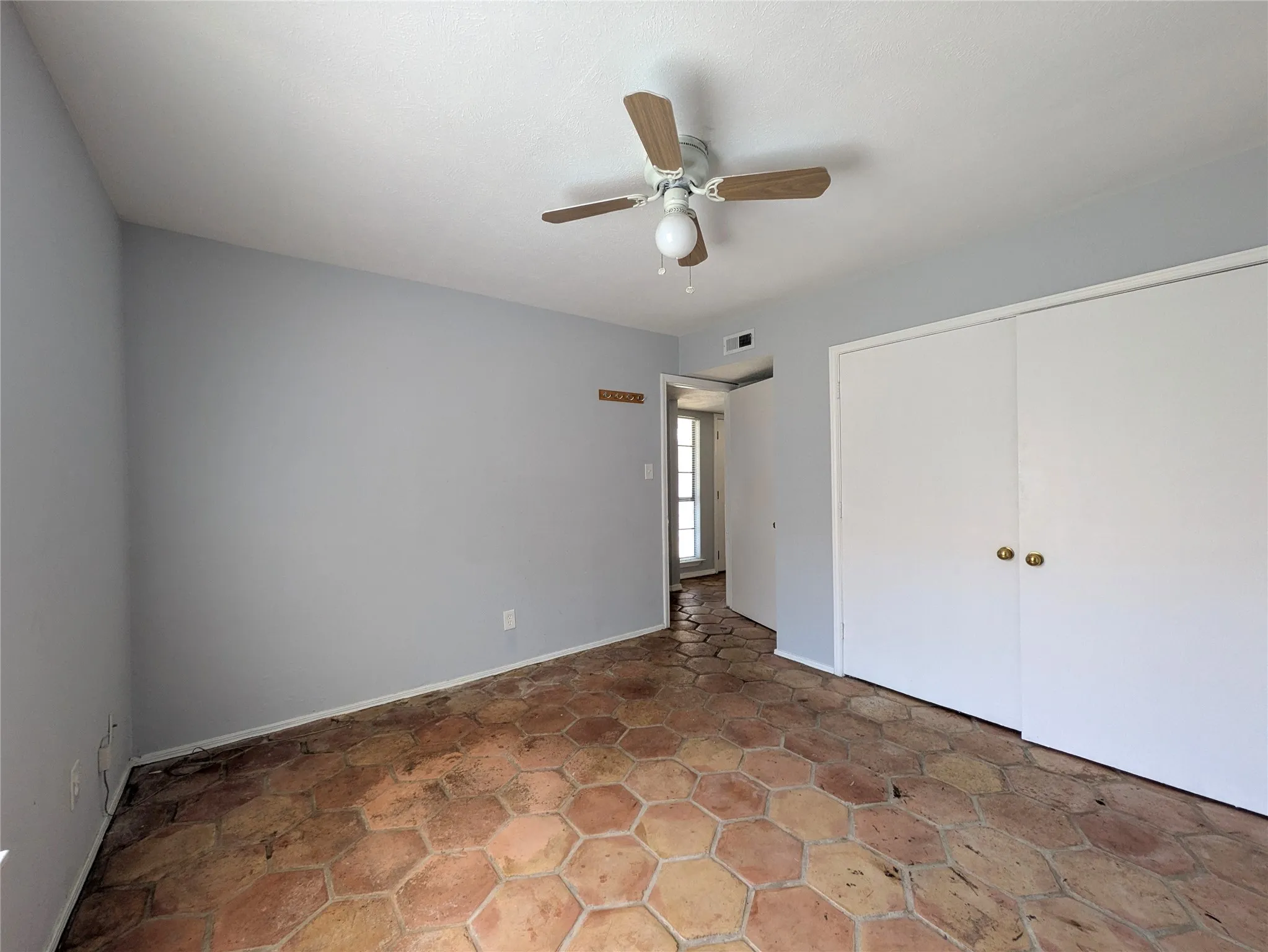 Hexagonal tile flooring, neutral wall color, ceiling fan with light fixture, and double sliding closet doors