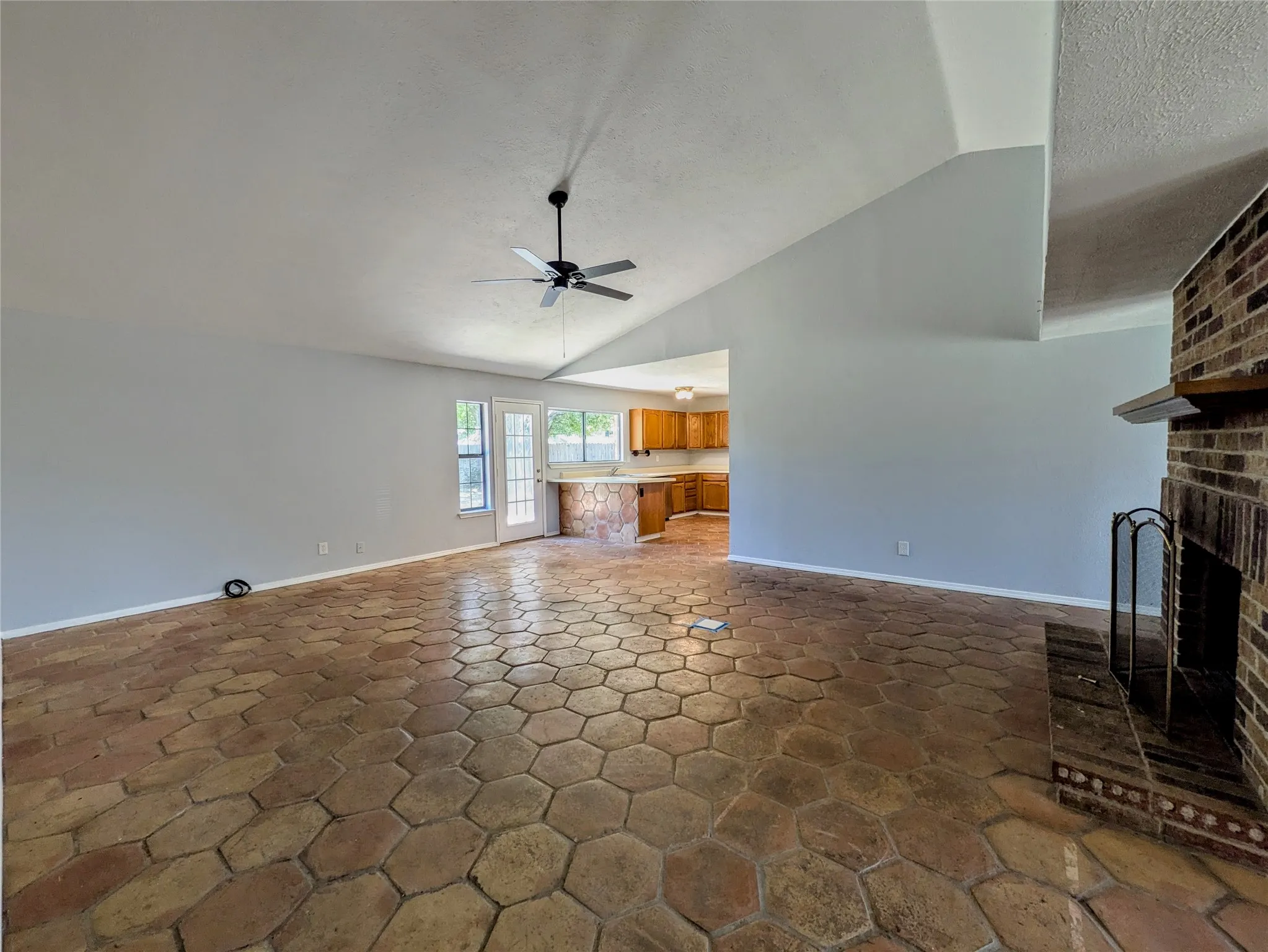 Vaulted ceiling with a ceiling fan, brick fireplace with a wood mantel, hexagon tile flooring, and a French door with glass panels