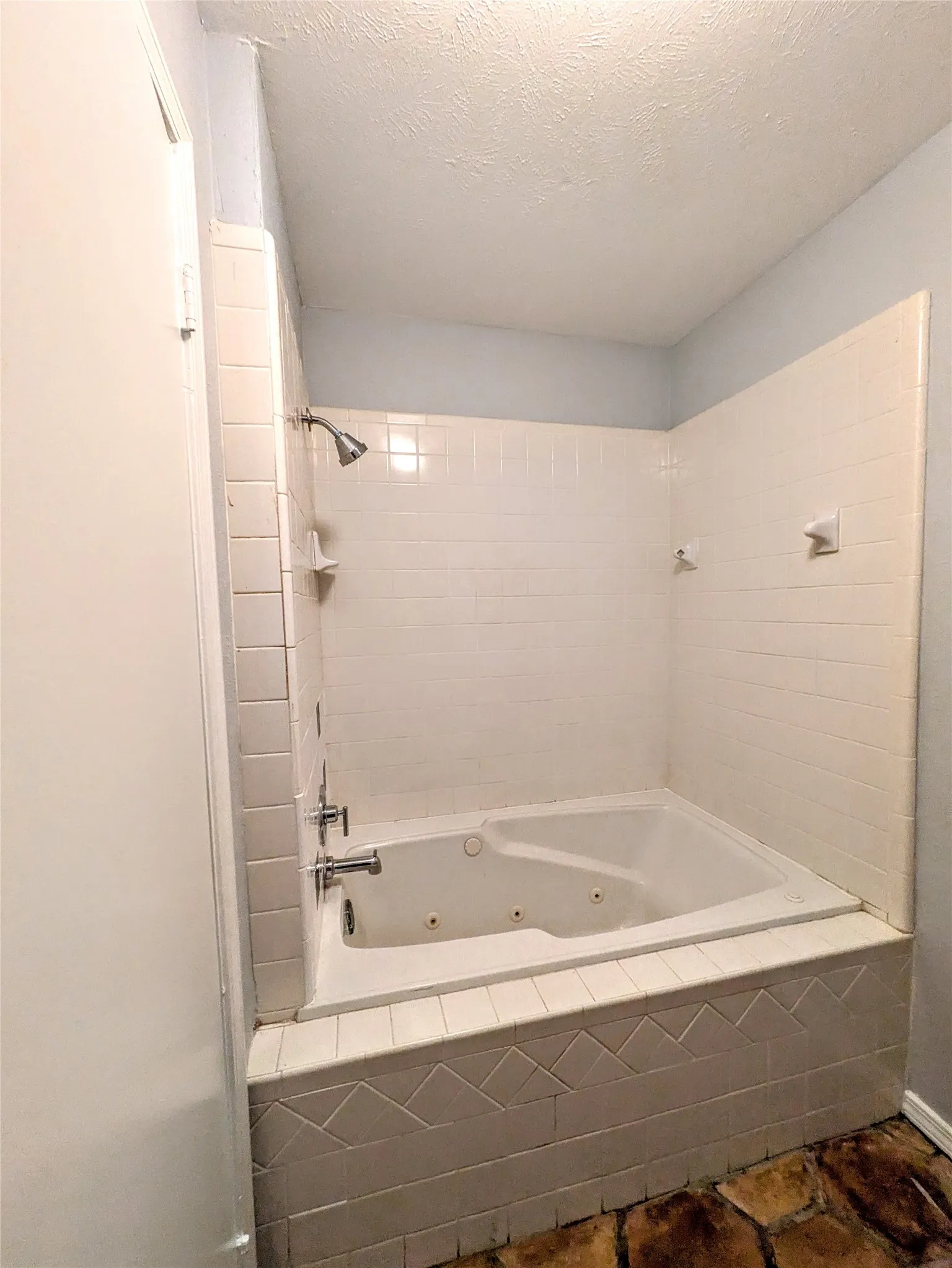 Built-in jetted tub with tiled surround, white subway tile shower, and wall-mounted shower head with faucet