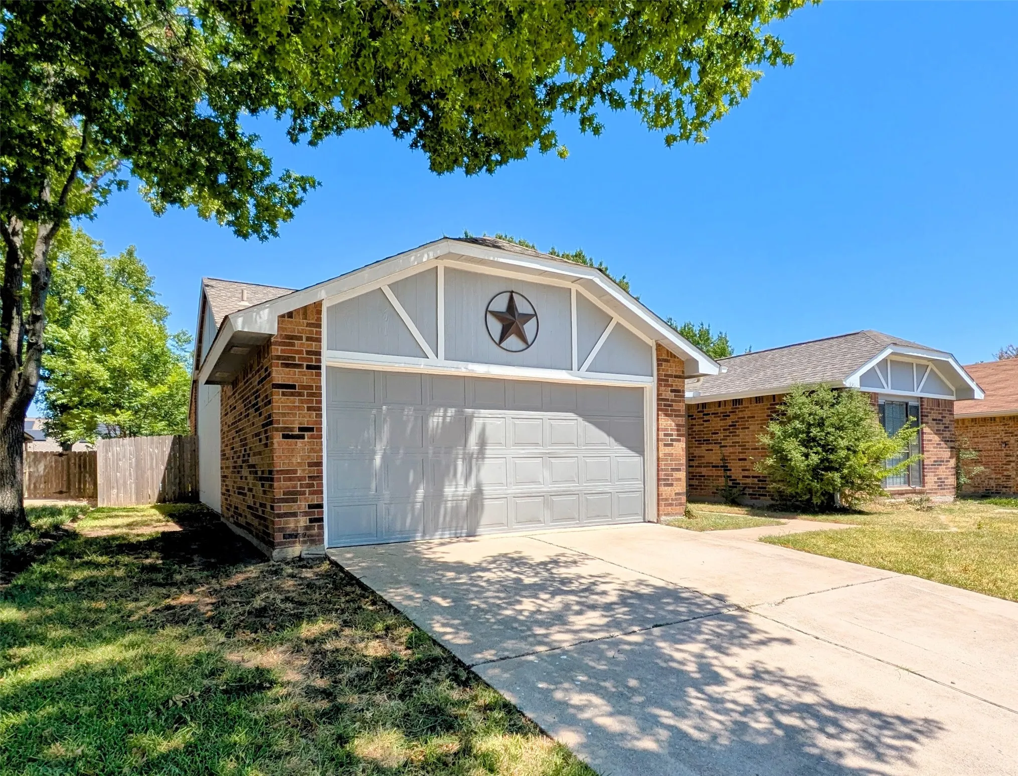 Brick exterior with light gray siding, attached garage, concrete driveway, and a front lawn with mature trees