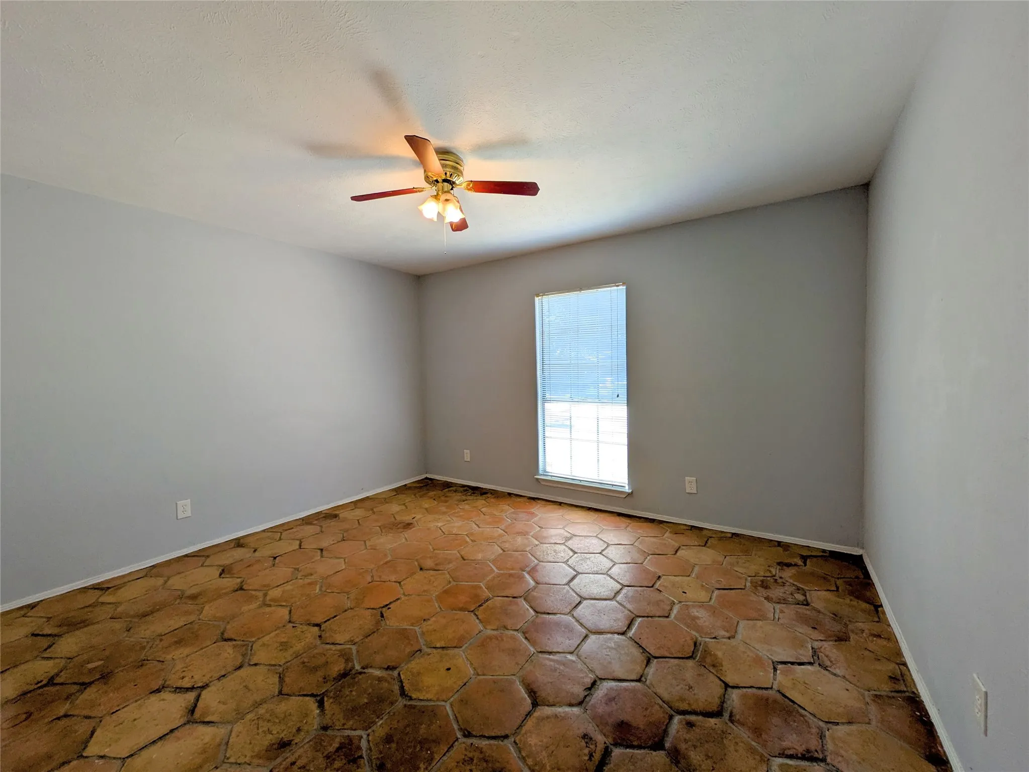 Hexagonal terracotta tile flooring, window with blinds, and ceiling fan with integrated lighting