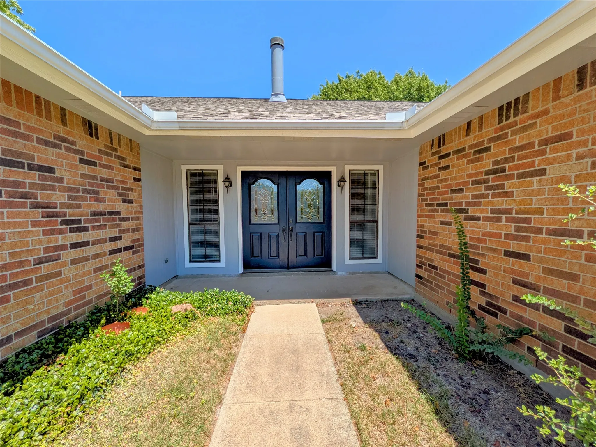 Brick facade with a covered entry, double entry doors featuring decorative glass inserts, and two flanking windows with white trim