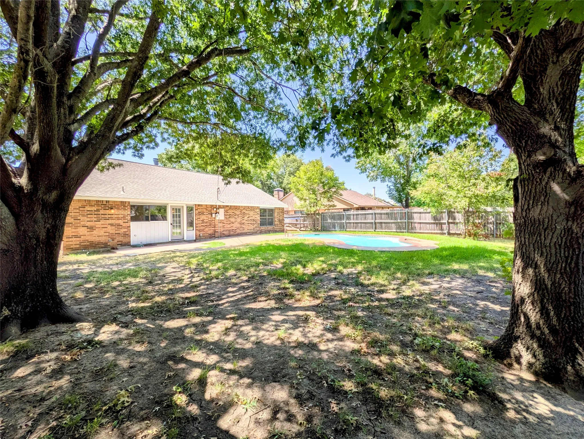 Expansive backyard featuring a blue-tiled pool, a wooden privacy fence, and mature trees providing shade